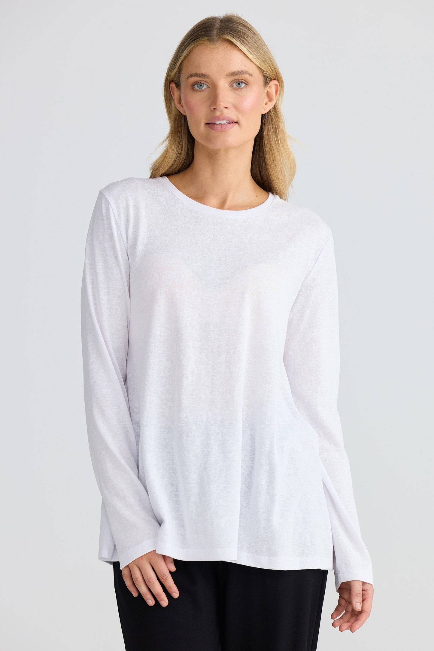 Woman wearing a white long-sleeve top and black pants on a light gray background