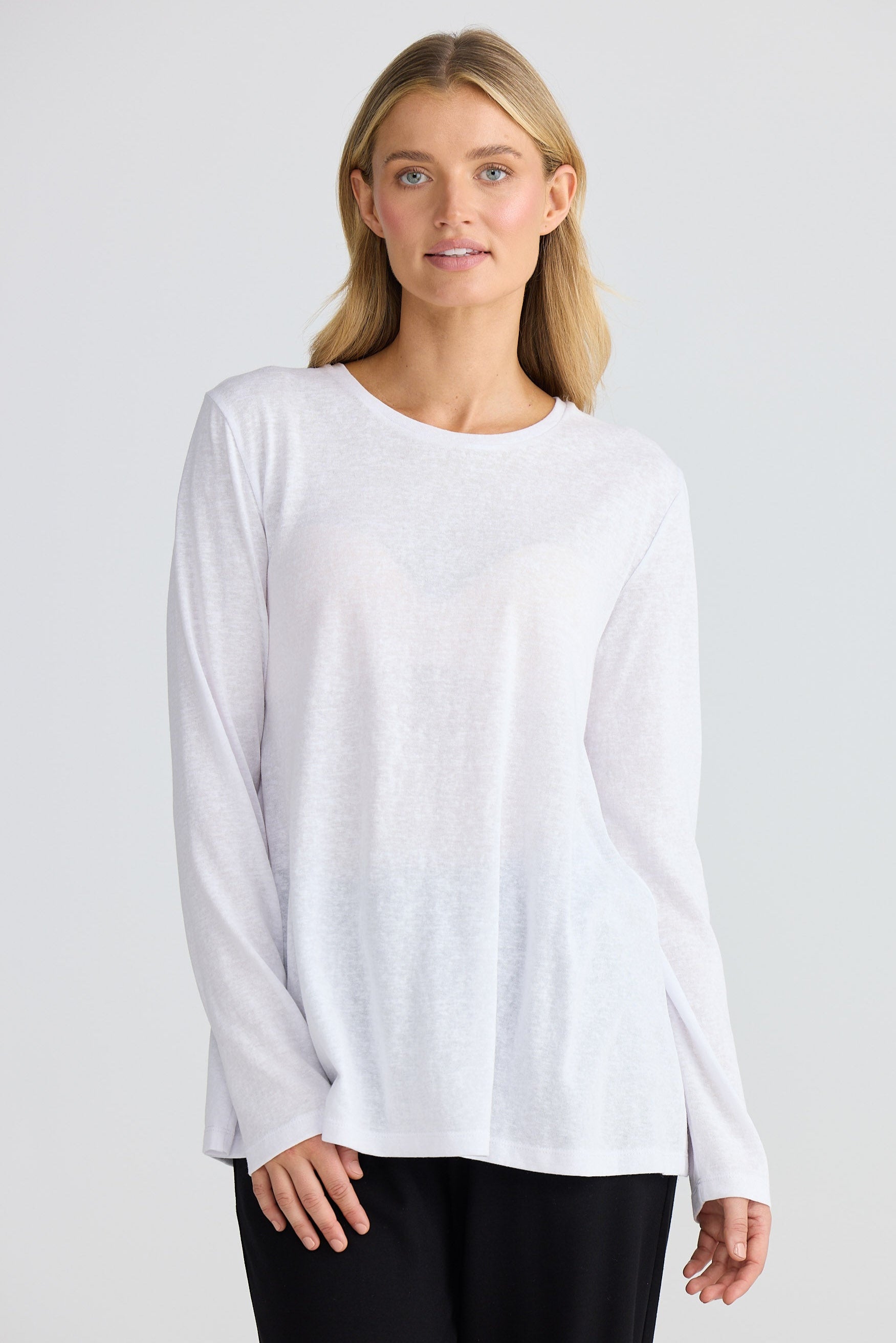 Woman wearing a white long-sleeve top and black pants on a light gray background