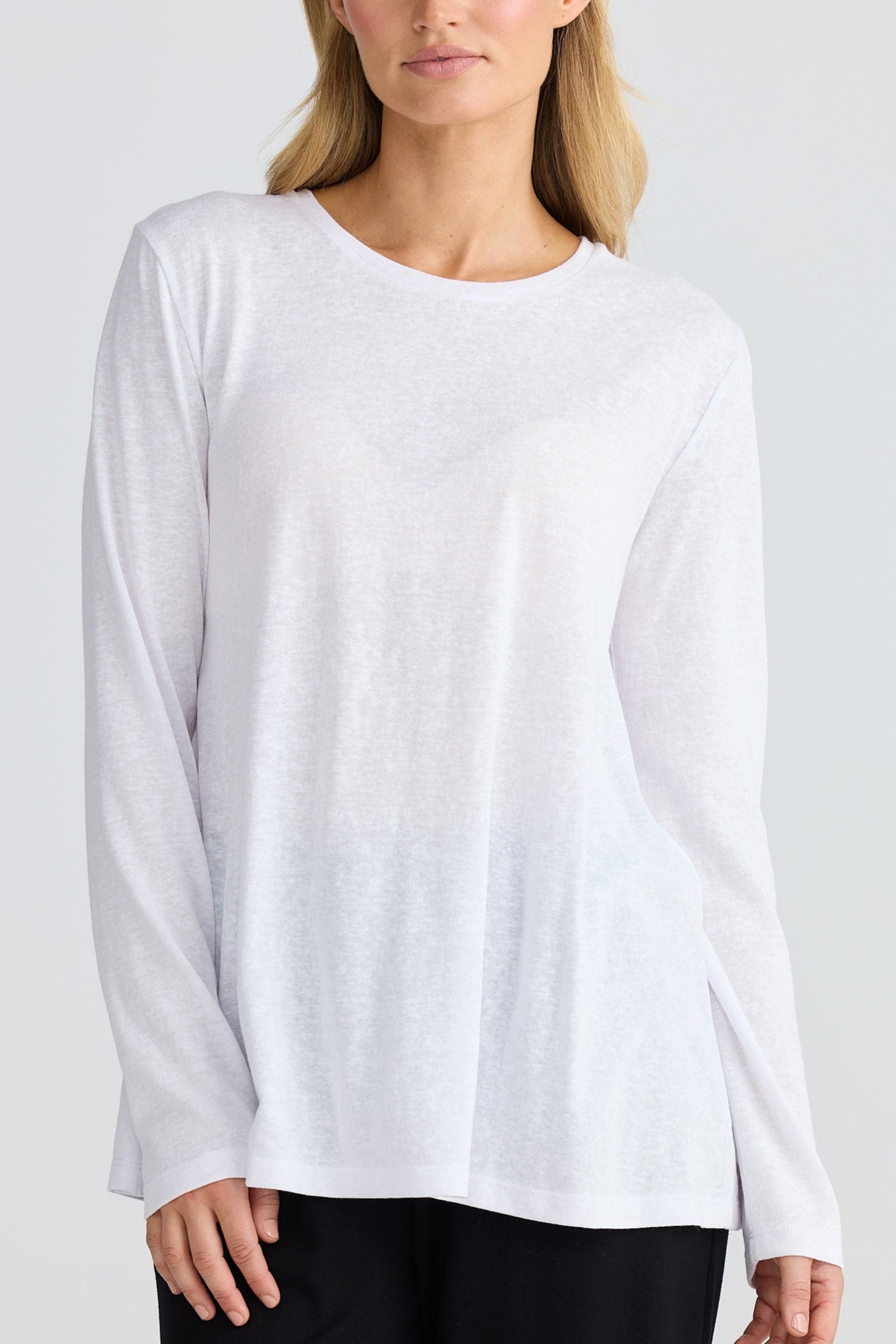 Woman wearing a white long-sleeve top and black pants on a light gray background