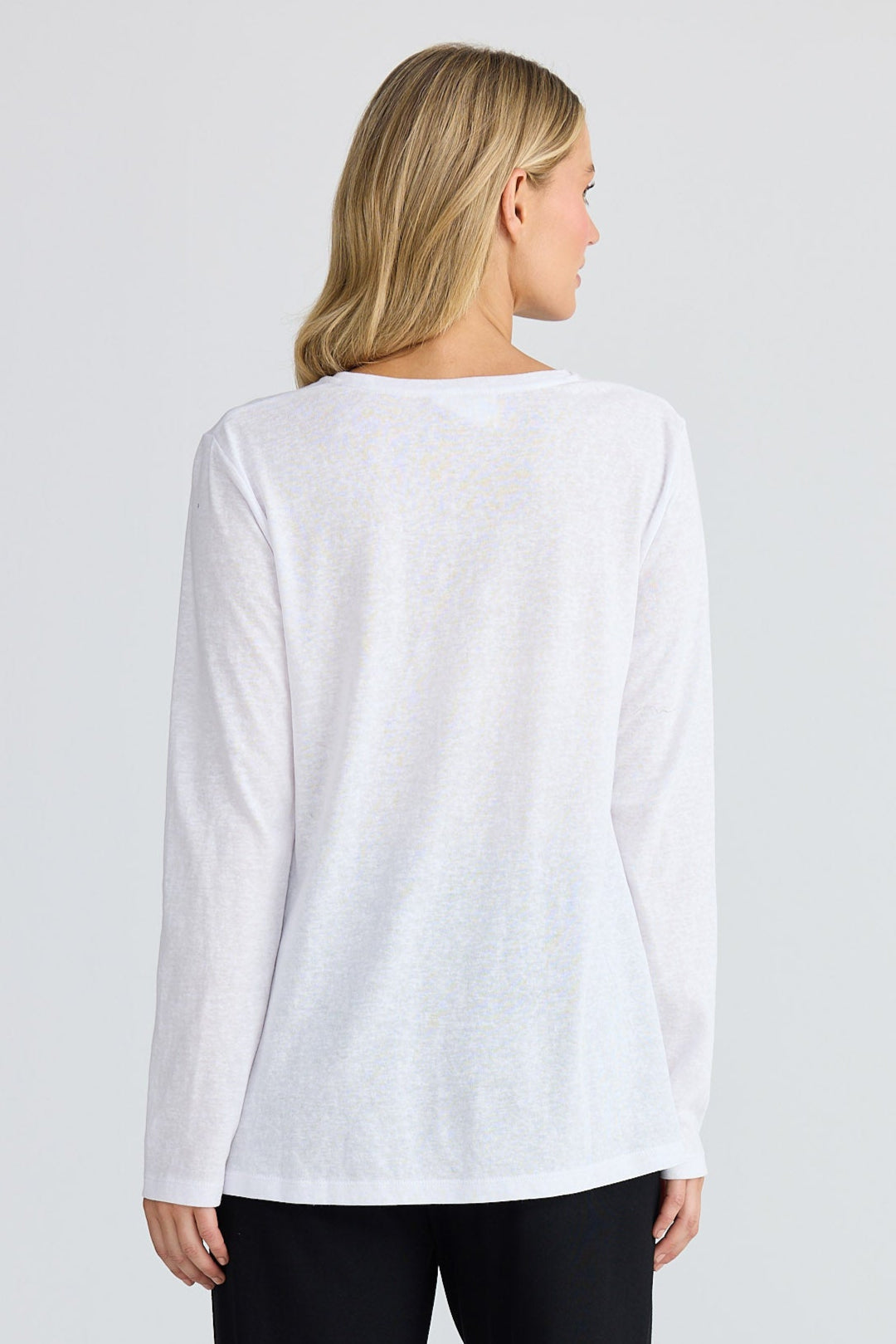 Woman wearing a white long sleeve top and black pants on a plain background