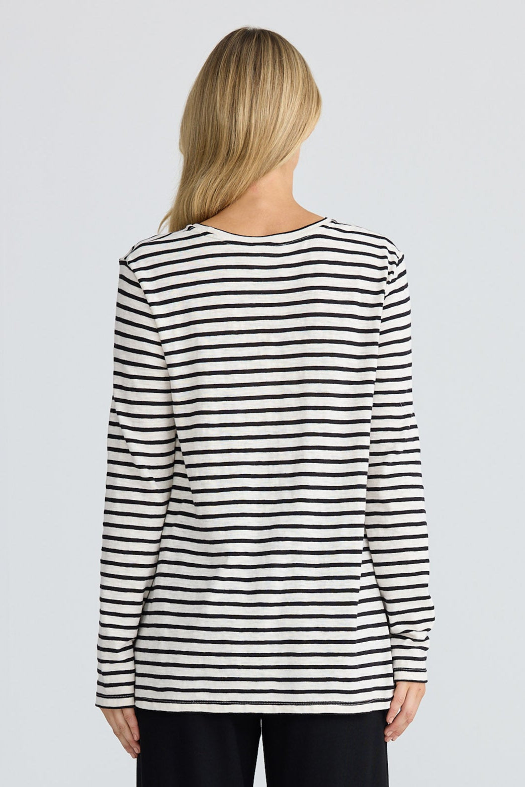 Person wearing a black and white striped long-sleeve top and black pants on a white background