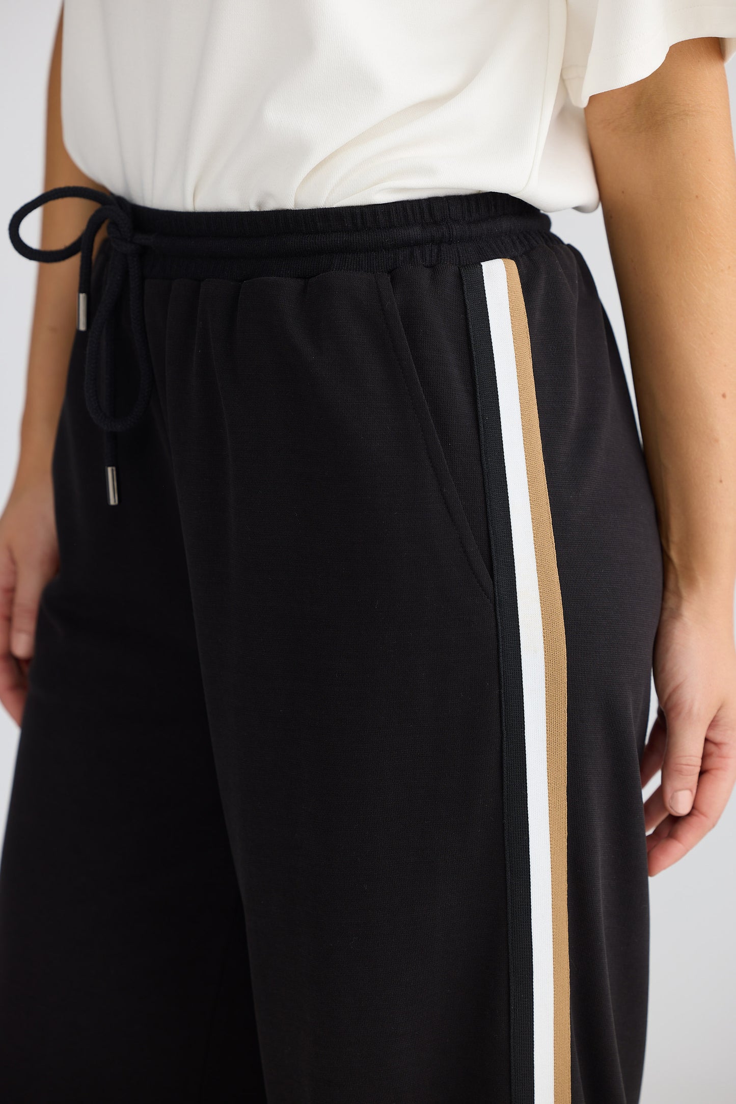 Black pants with a white stripe on a person wearing a white top against a light background