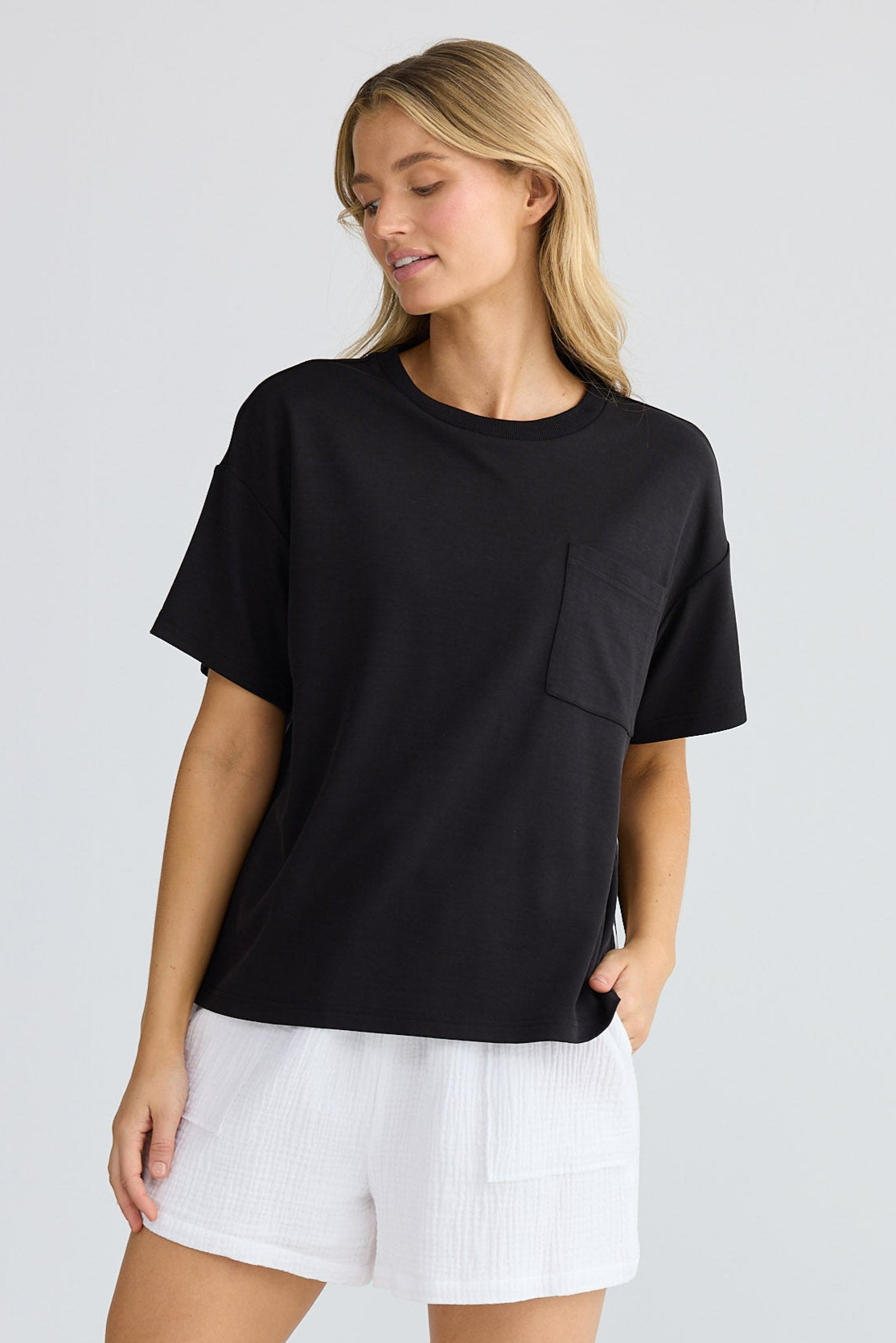 Woman wearing a black t-shirt, white shorts, and white sneakers on a light gray background