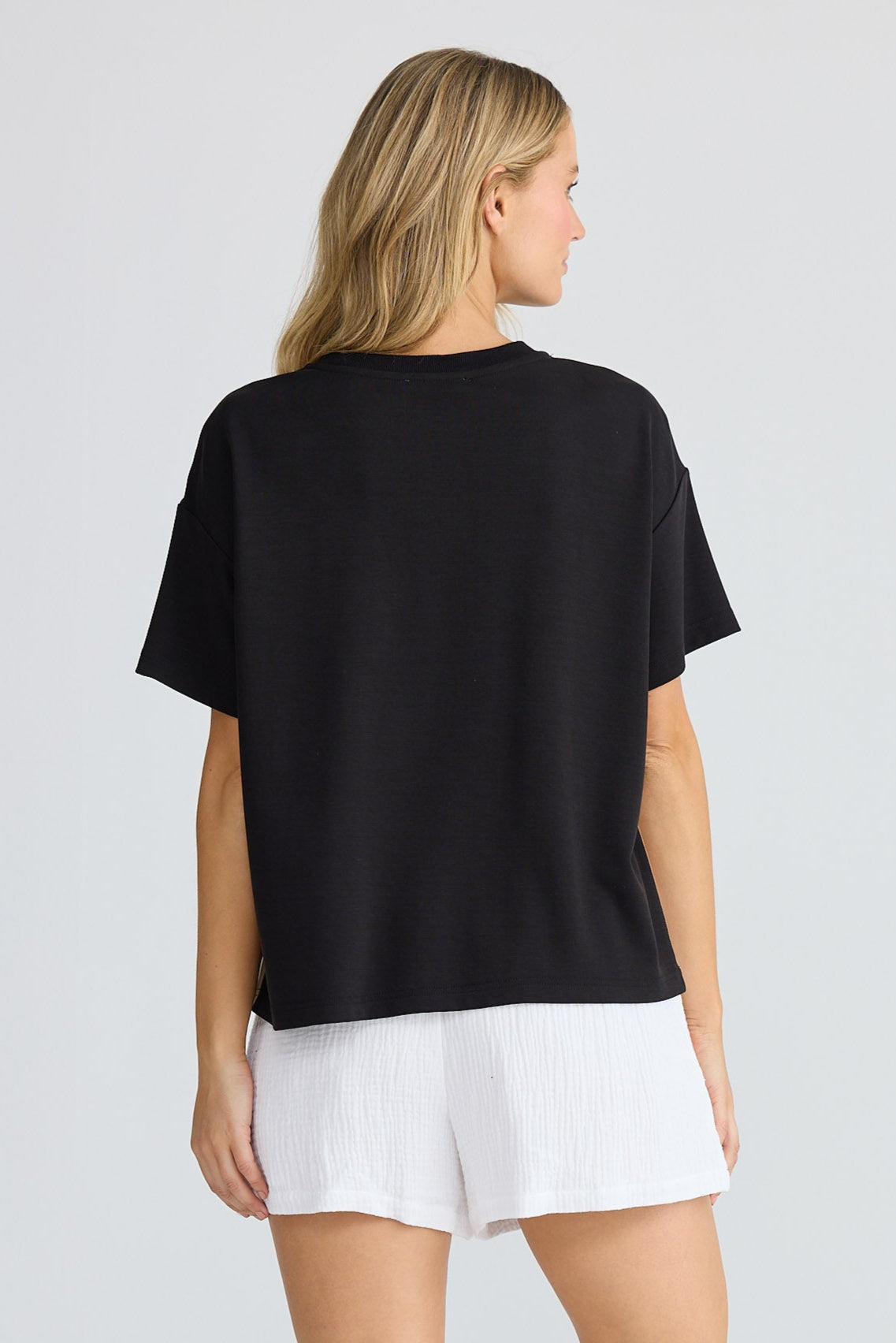 Person wearing a black t-shirt and white shorts on a plain background