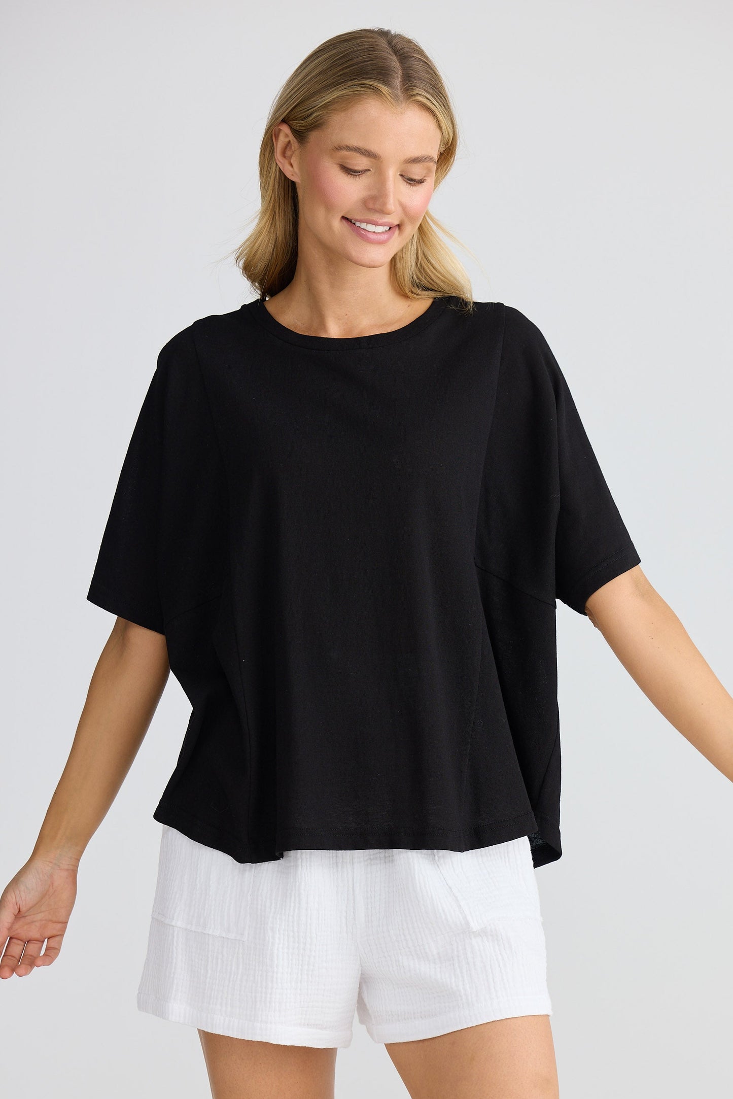Woman wearing a black oversized top and white shorts on a plain background