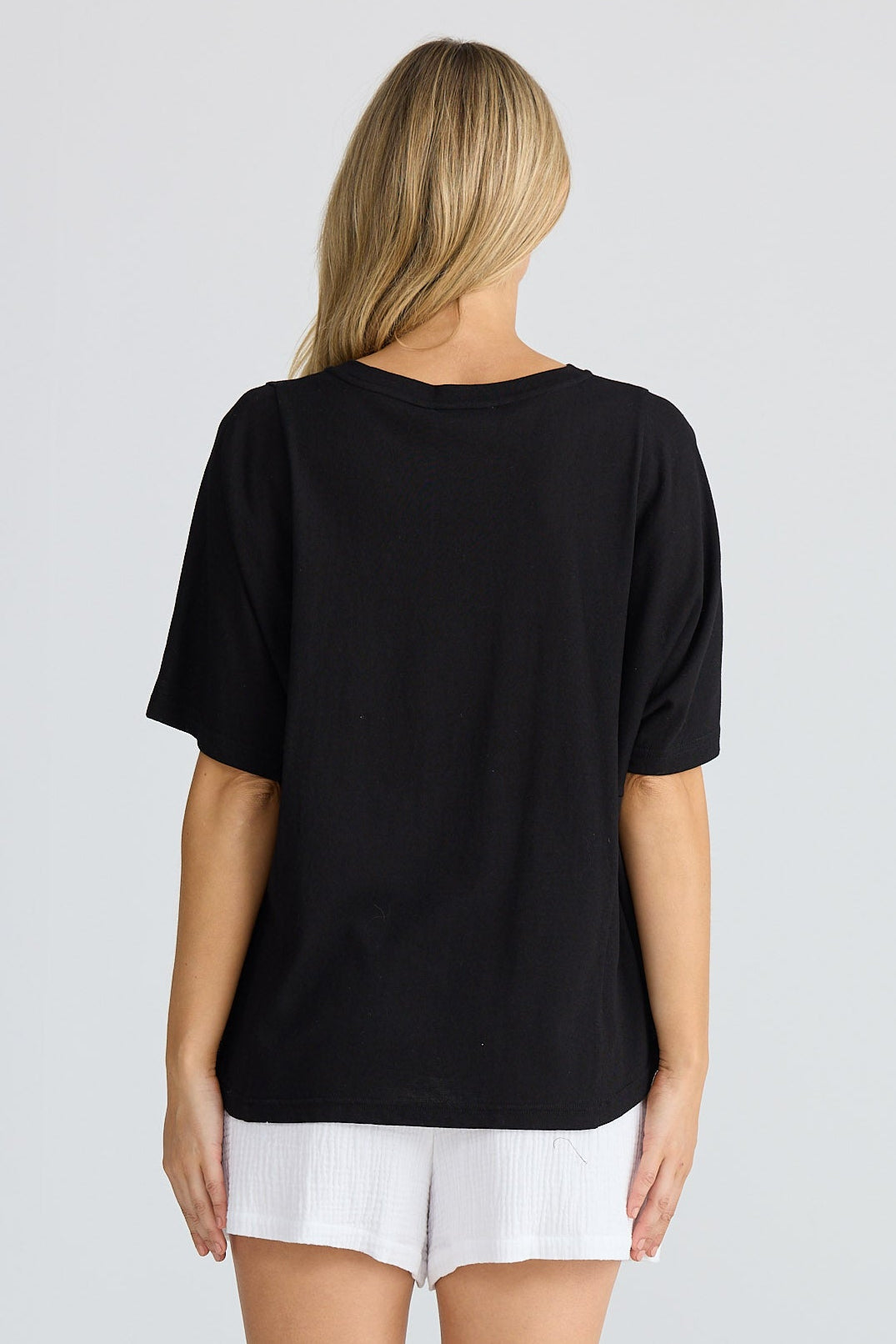 Person wearing a black t-shirt and white shorts on a plain background