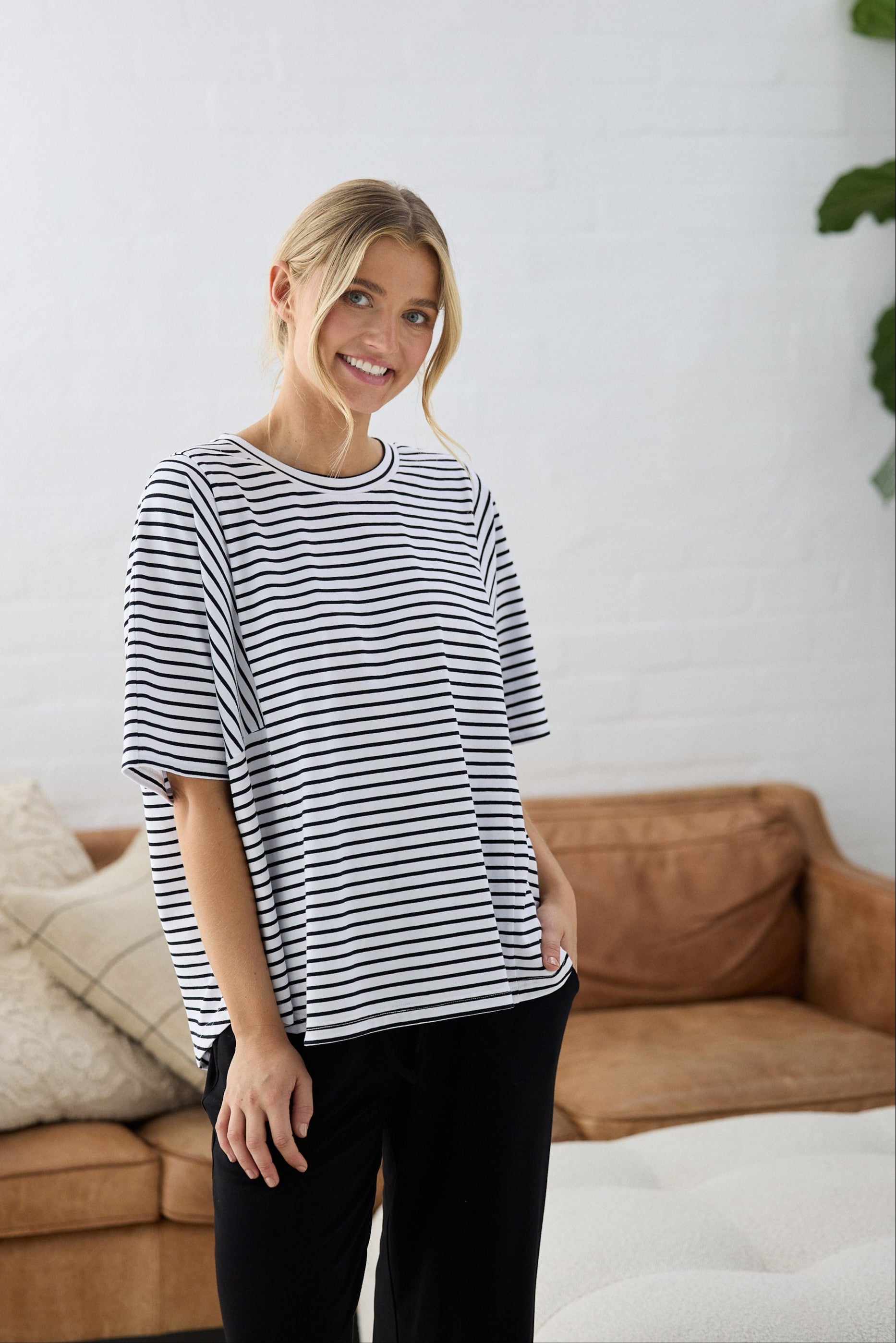 Woman wearing a striped shirt standing in a living room with a couch and plant.