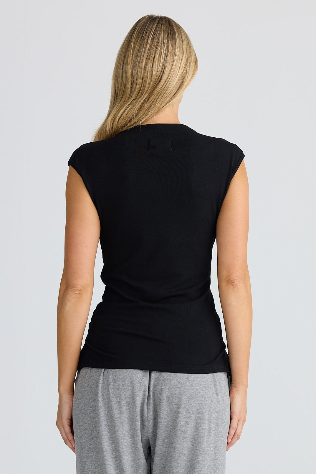 Woman wearing a black sleeveless top and gray pants on a white background