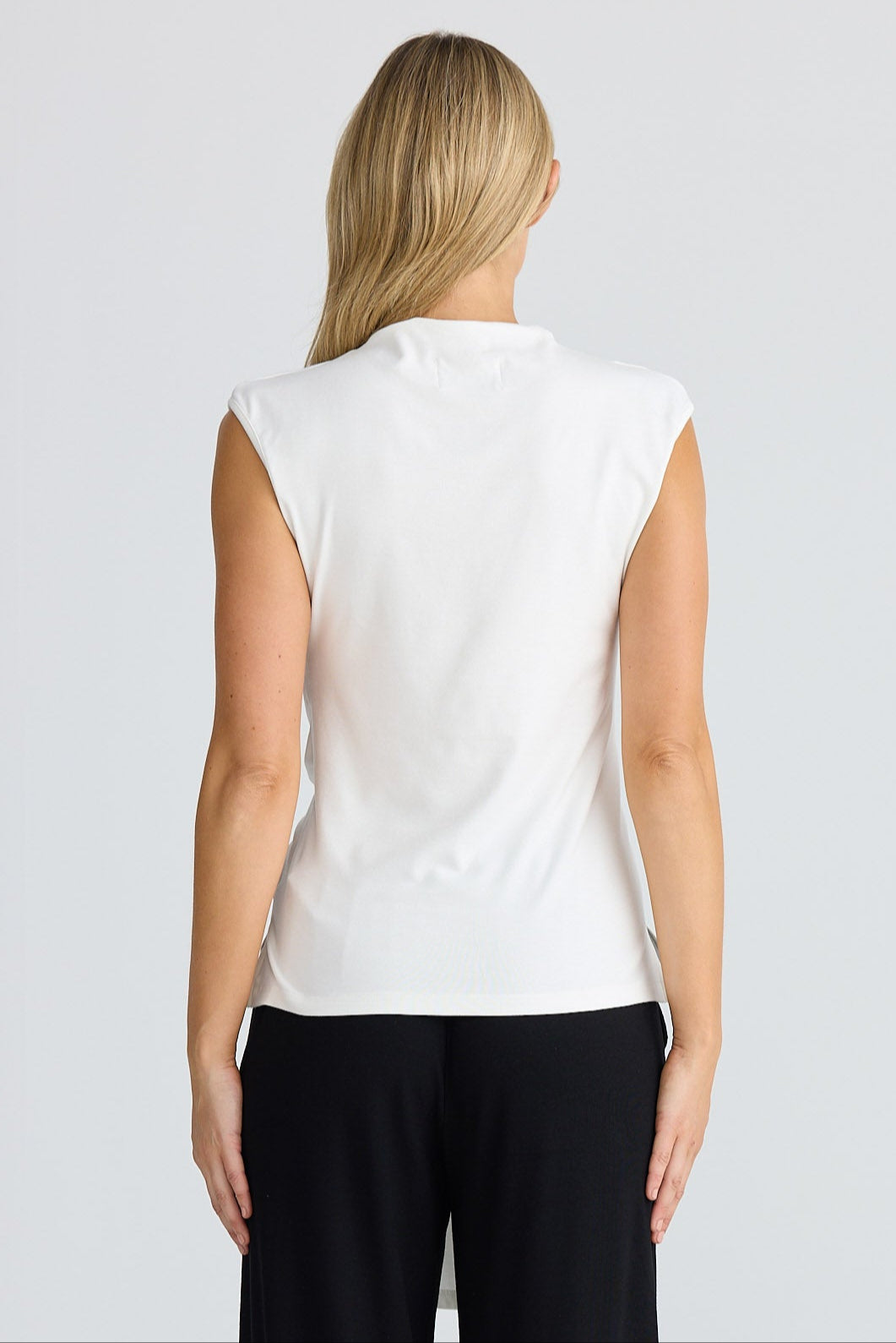 Person wearing a white sleeveless top and black pants on a plain background