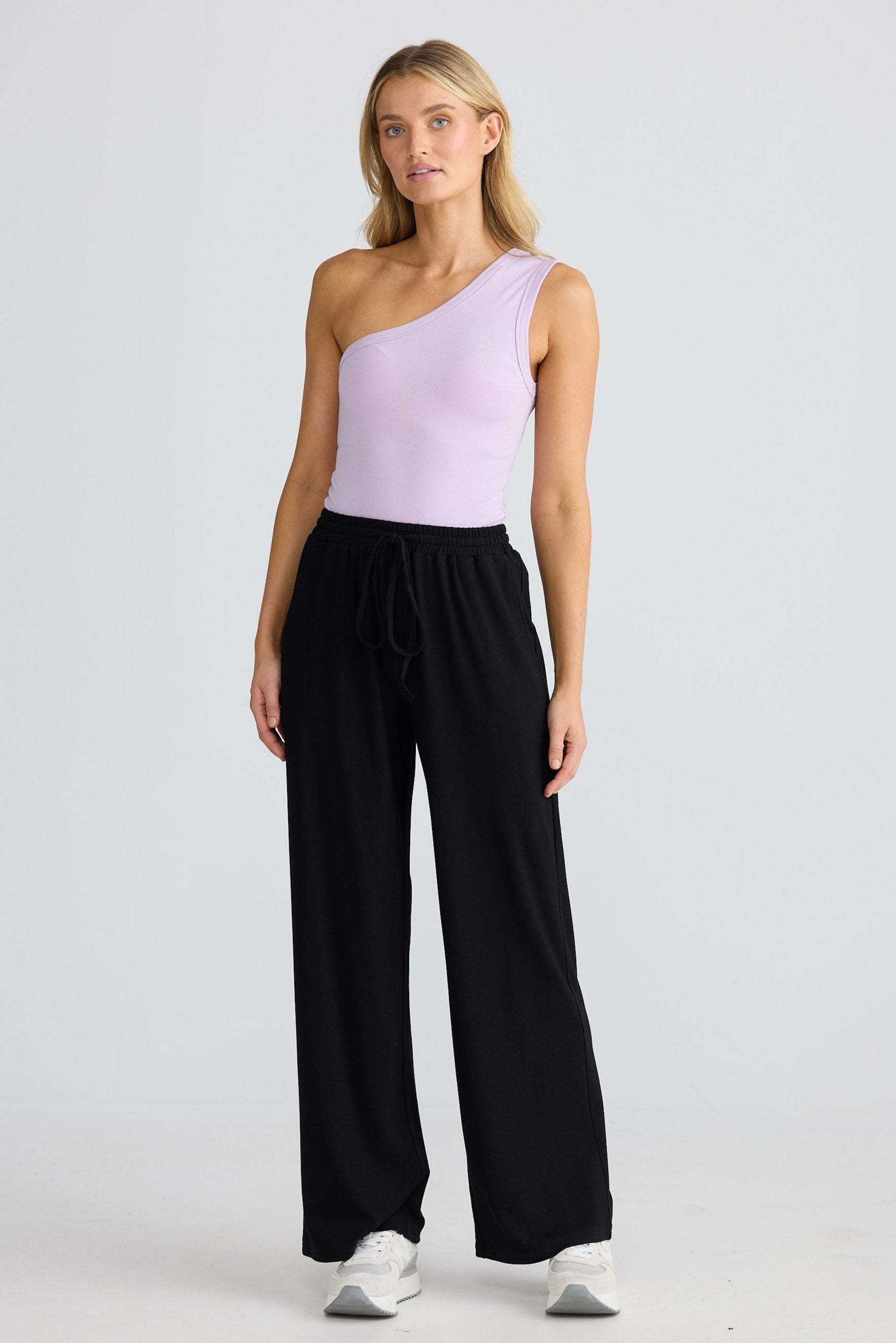 Woman wearing a light purple one-shoulder top and black pants on a white background