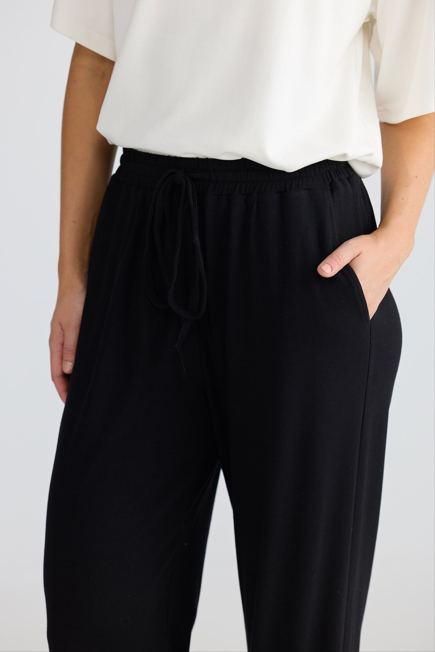 Person wearing black pants and a white top on a plain background