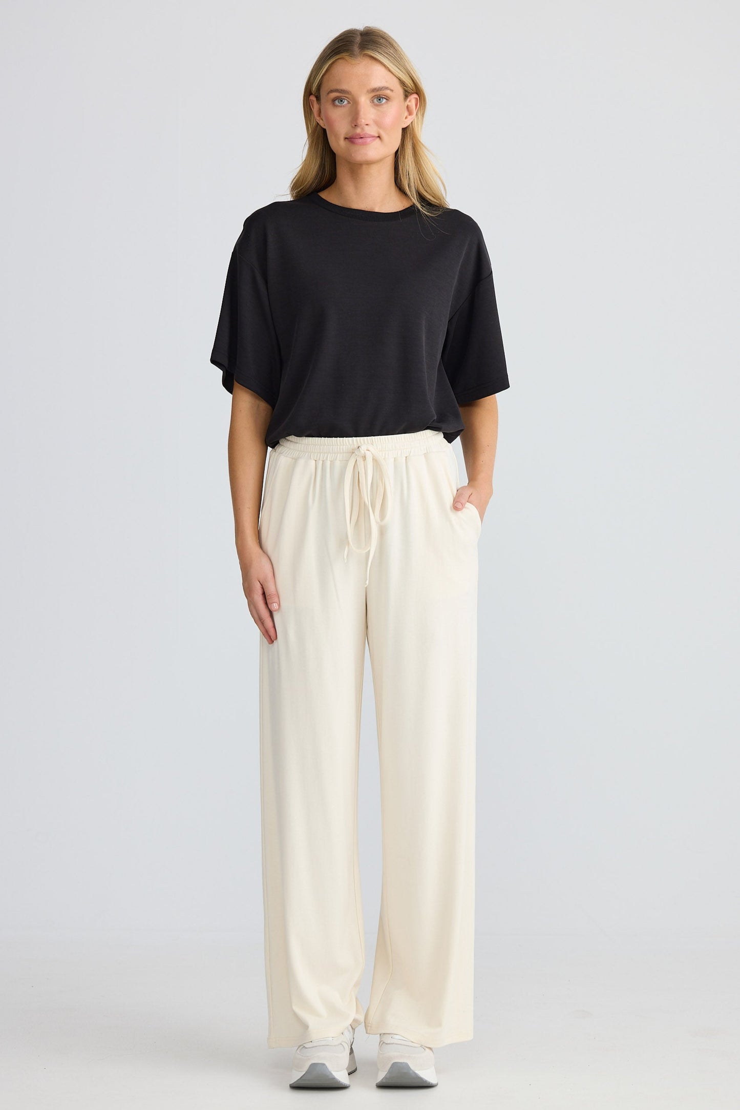 Woman wearing a black top and cream pants on a light gray background