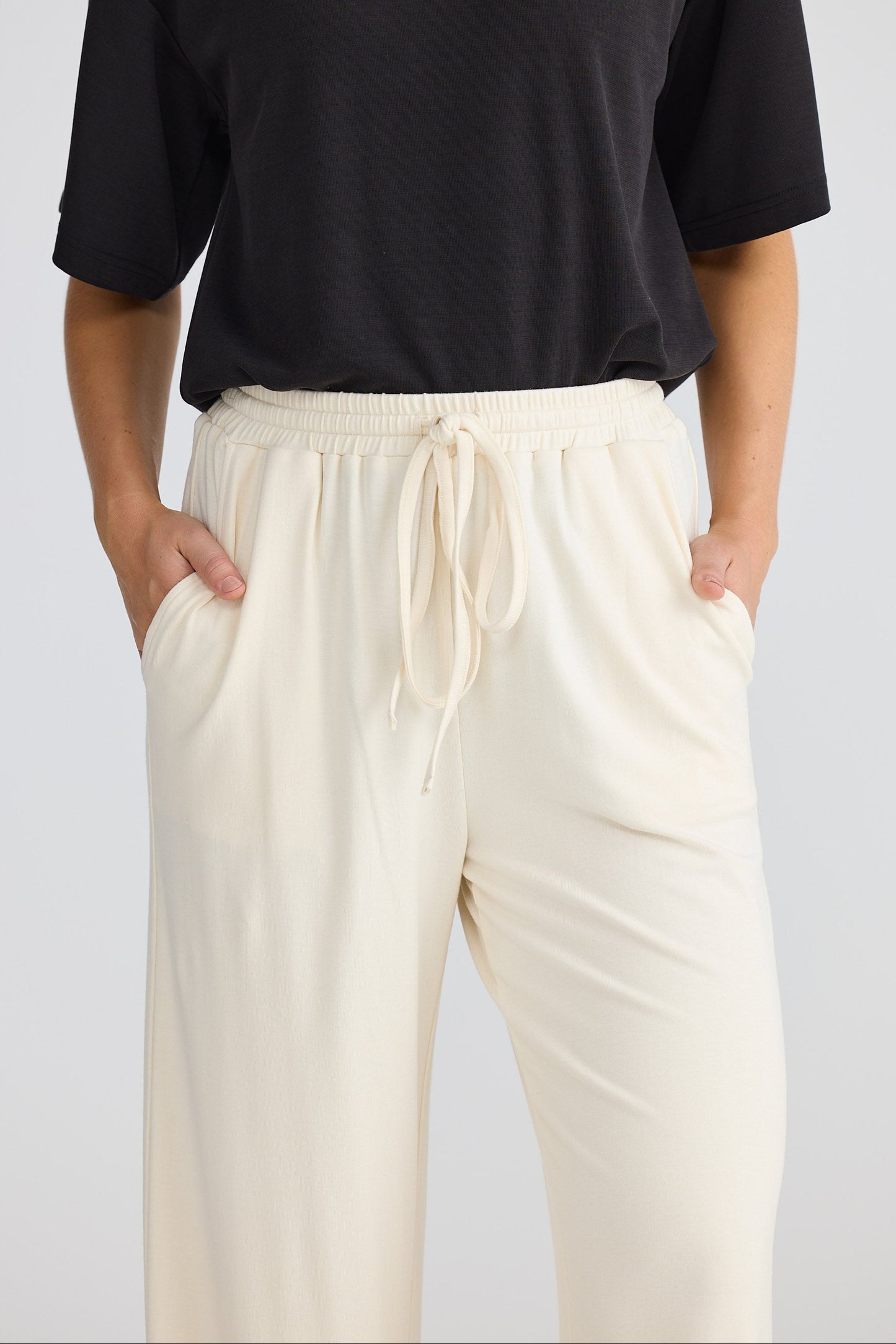Person wearing a black top and cream pants on a plain background