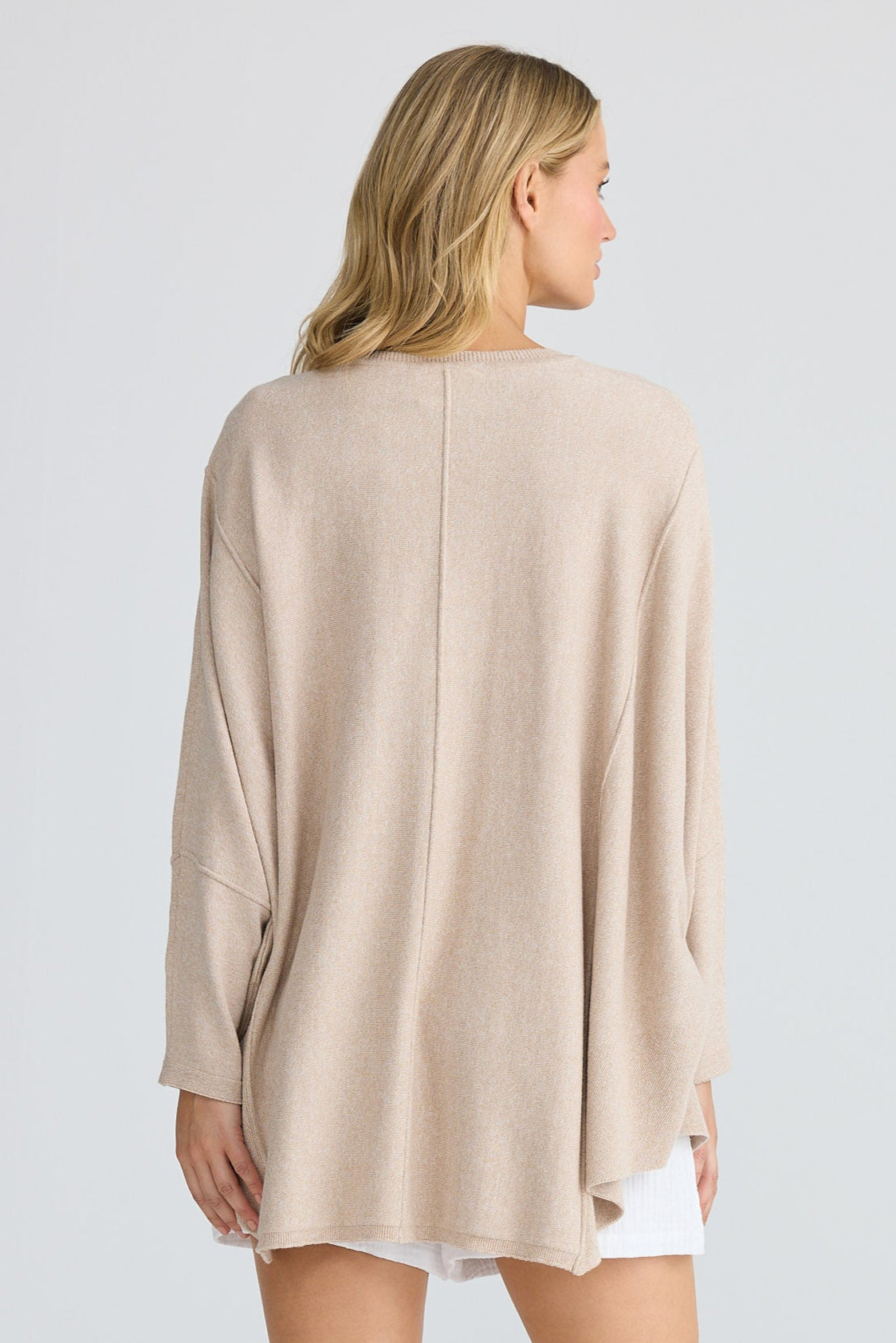 Woman wearing a beige long sleeve top over a white shirt on a plain background