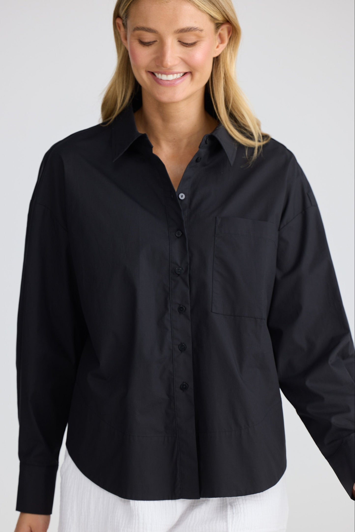 Woman wearing a black shirt and white pants on a plain background