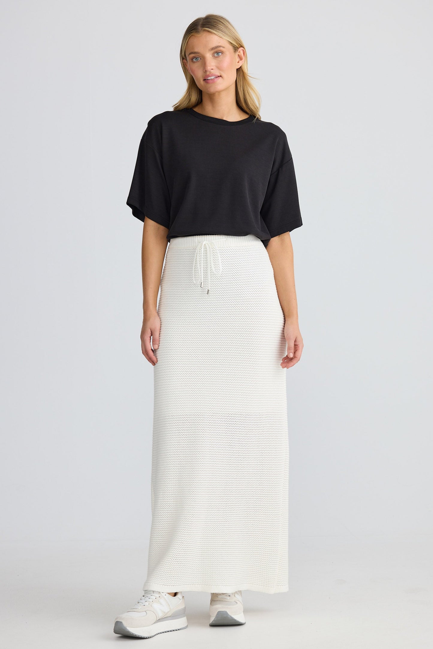 Woman wearing a black top and white skirt on a light gray background