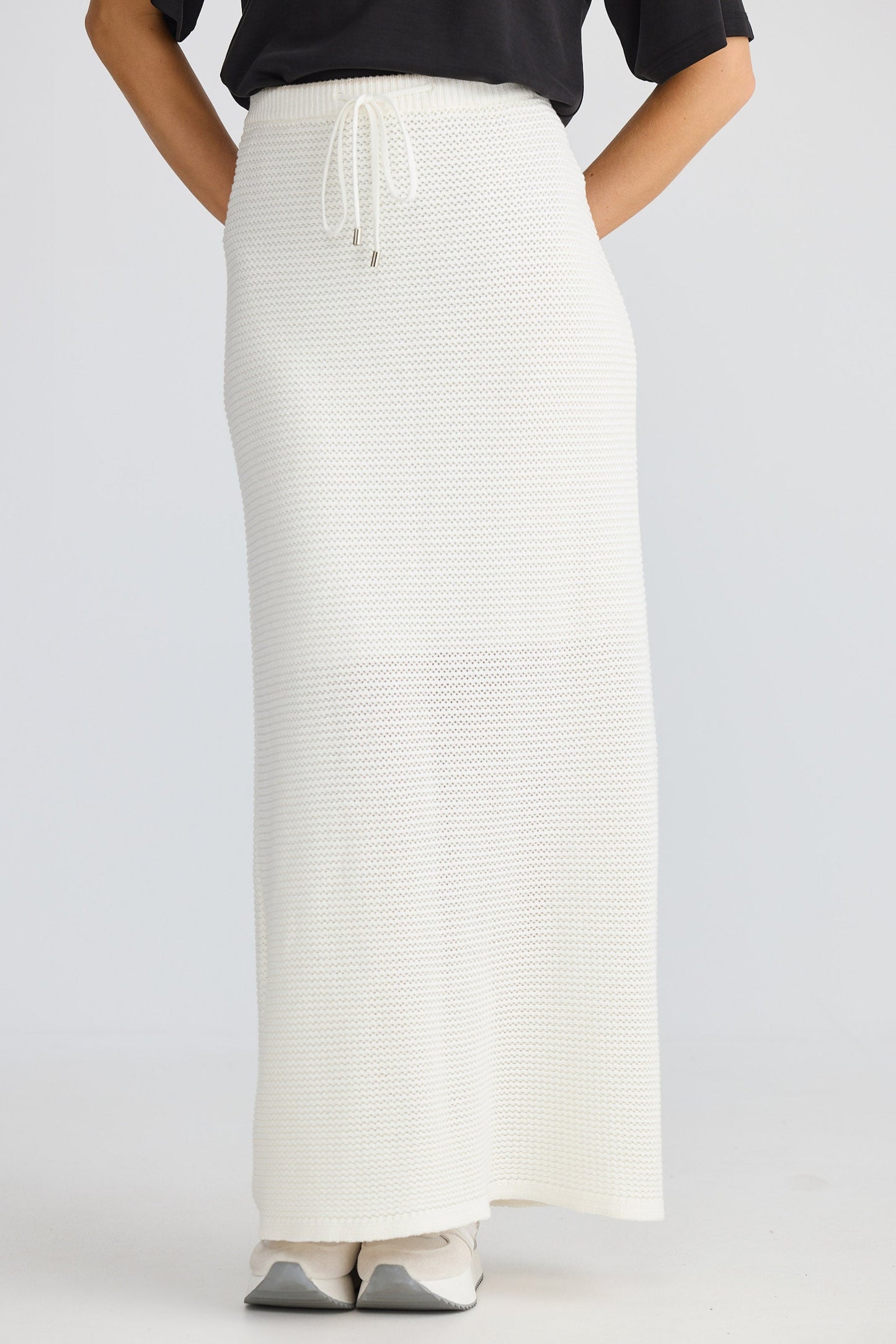 Person wearing a long white skirt with a black top on a light gray background