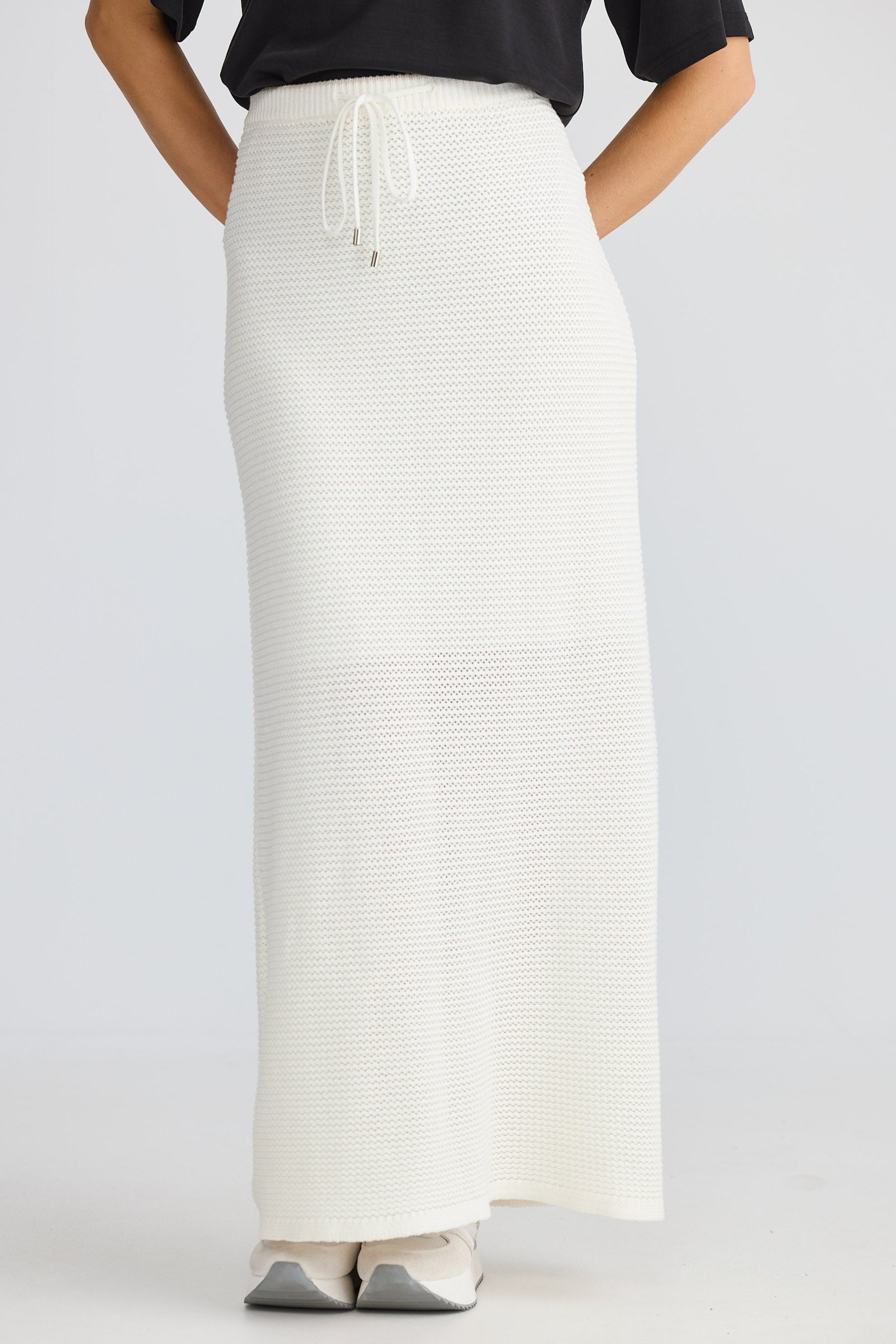 Person wearing a long white skirt with a black top on a light gray background