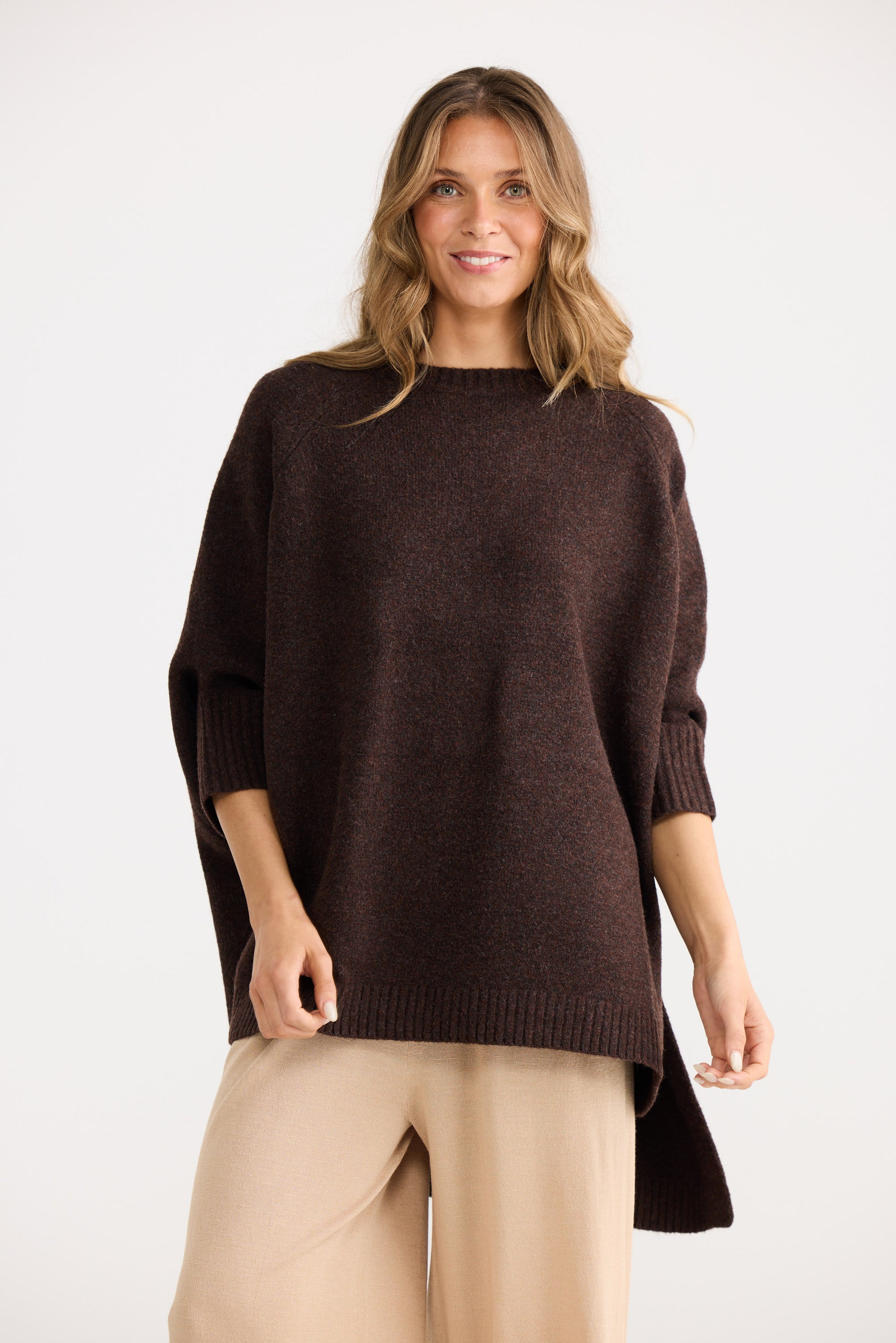 Woman wearing a brown sweater and beige pants on a white background