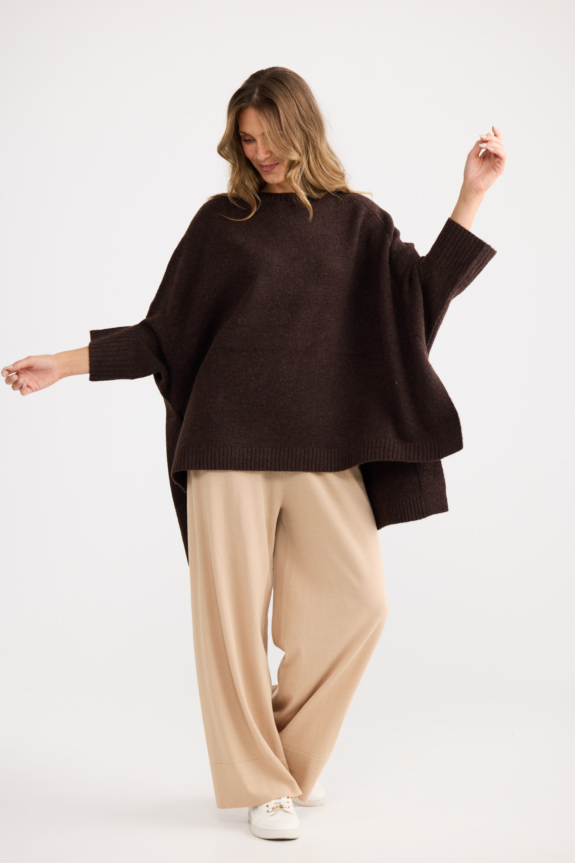 Woman wearing a brown sweater and beige pants on a white background