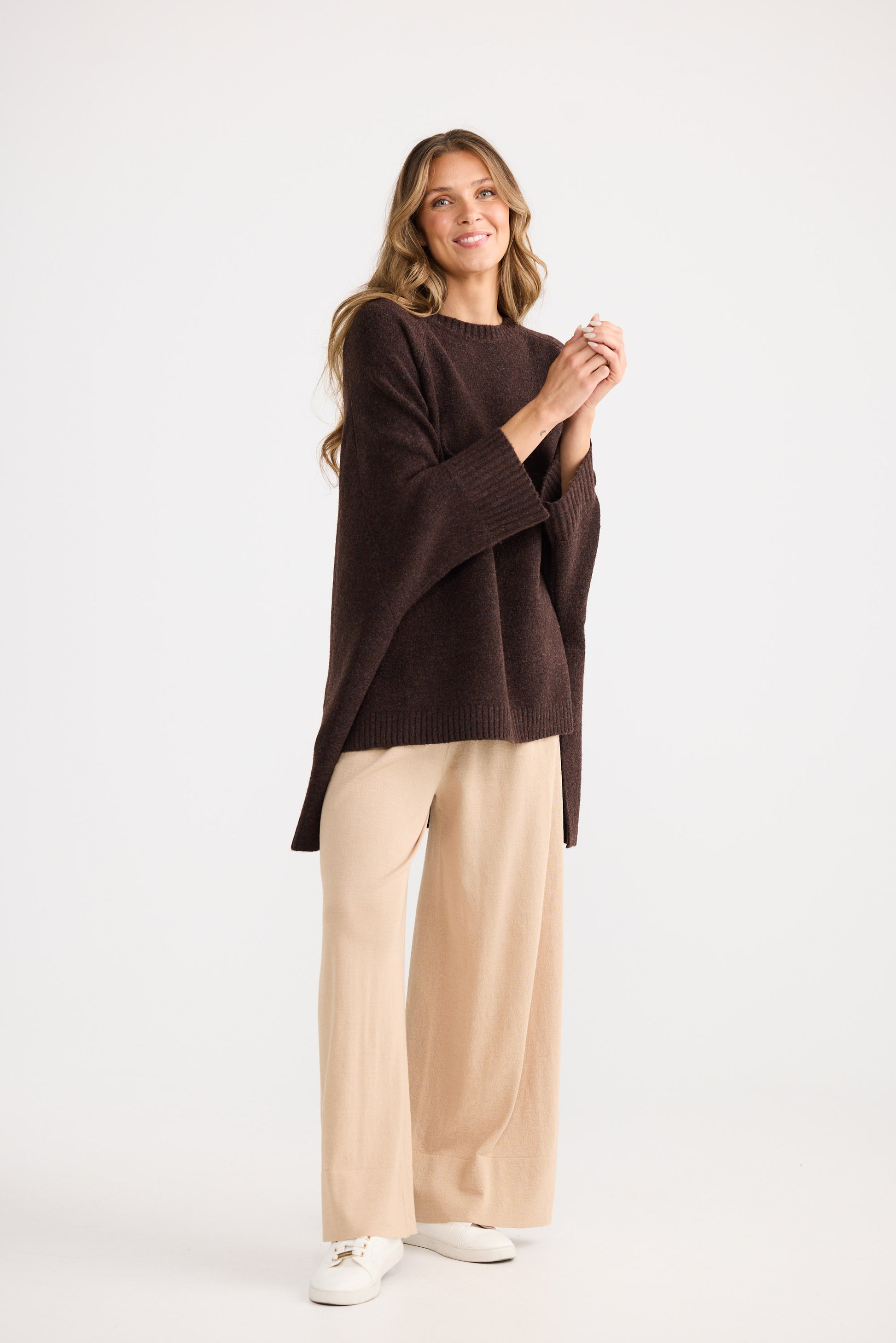 Woman wearing a brown poncho and beige pants on a white background