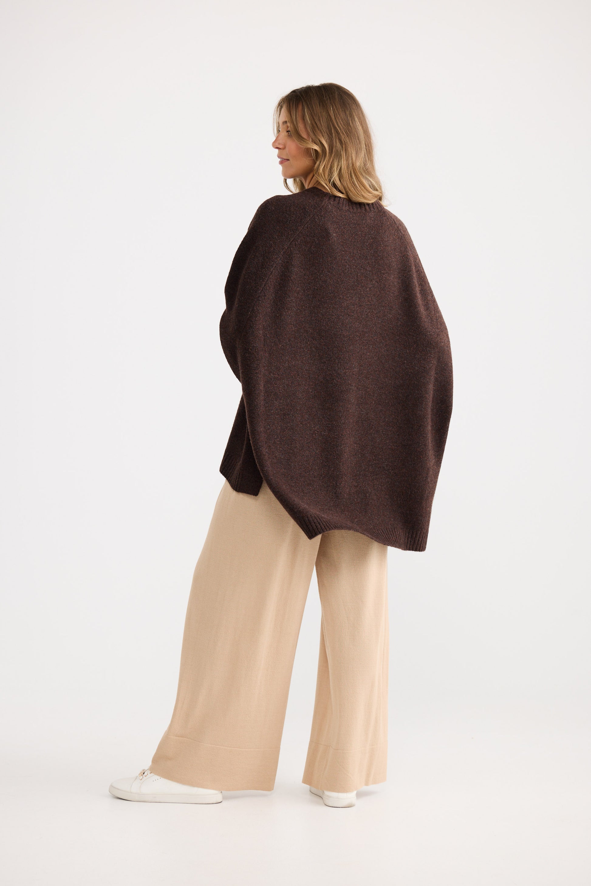 Woman wearing a brown poncho and beige pants on a white background