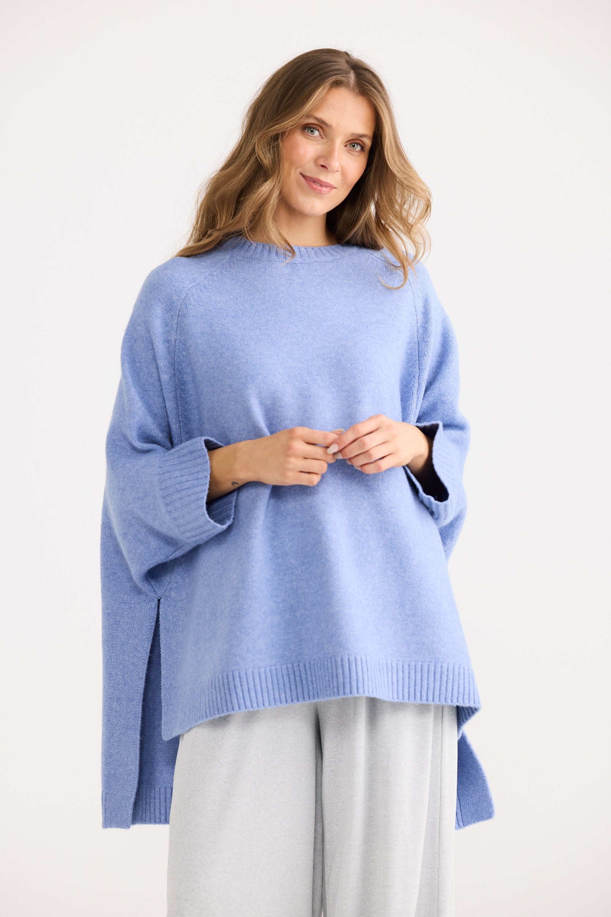 Woman wearing a blue sweater and grey pants on a white background