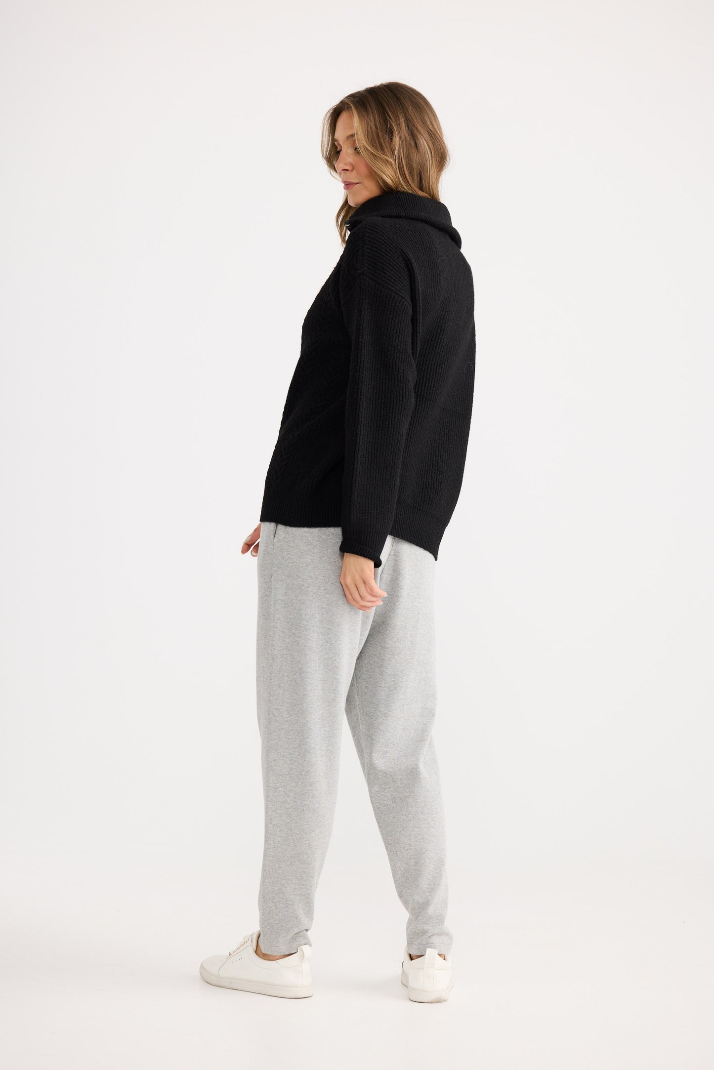 Woman wearing a black hoodie and gray pants on a white background