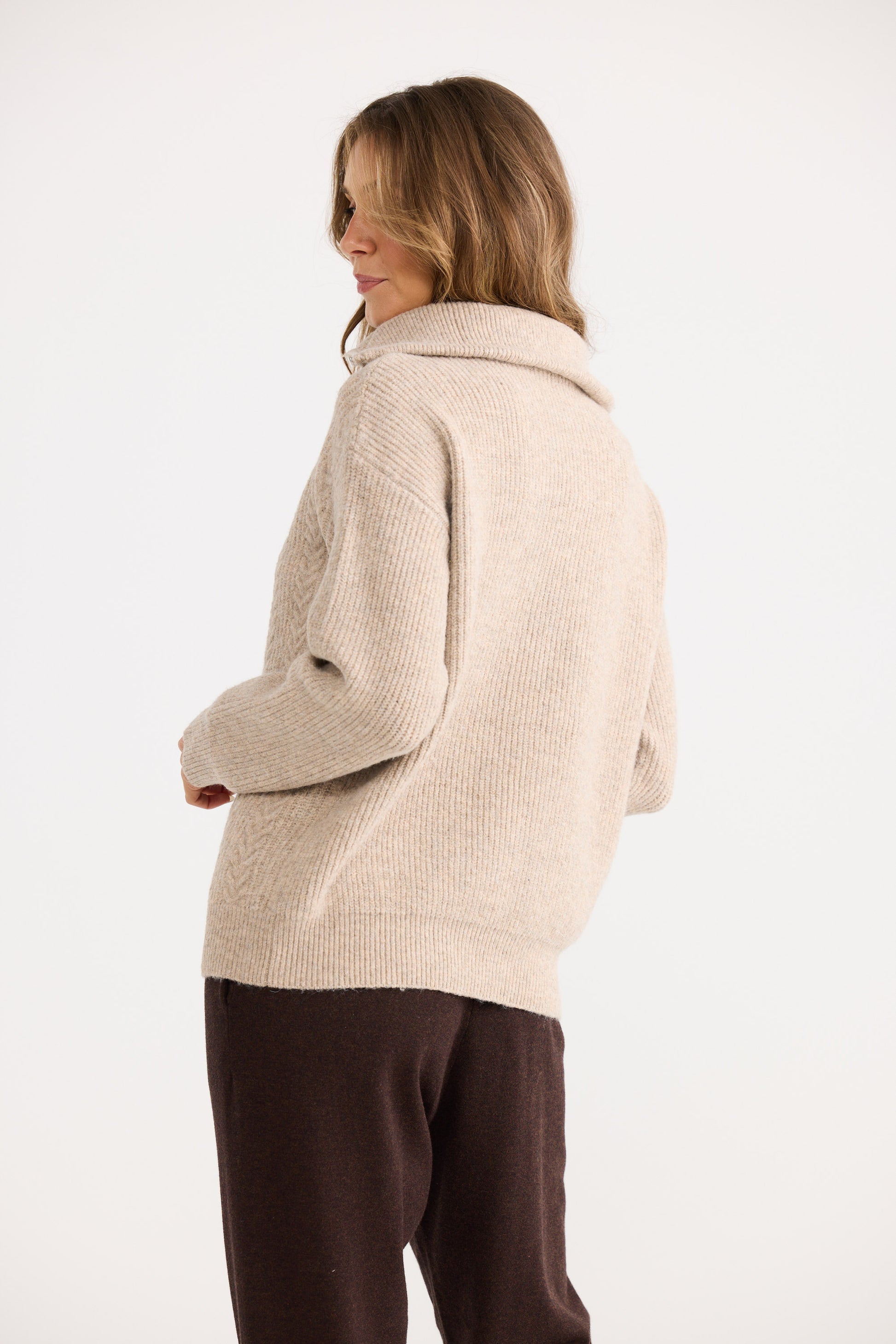 Woman wearing a beige knitted sweater and brown pants on a white background