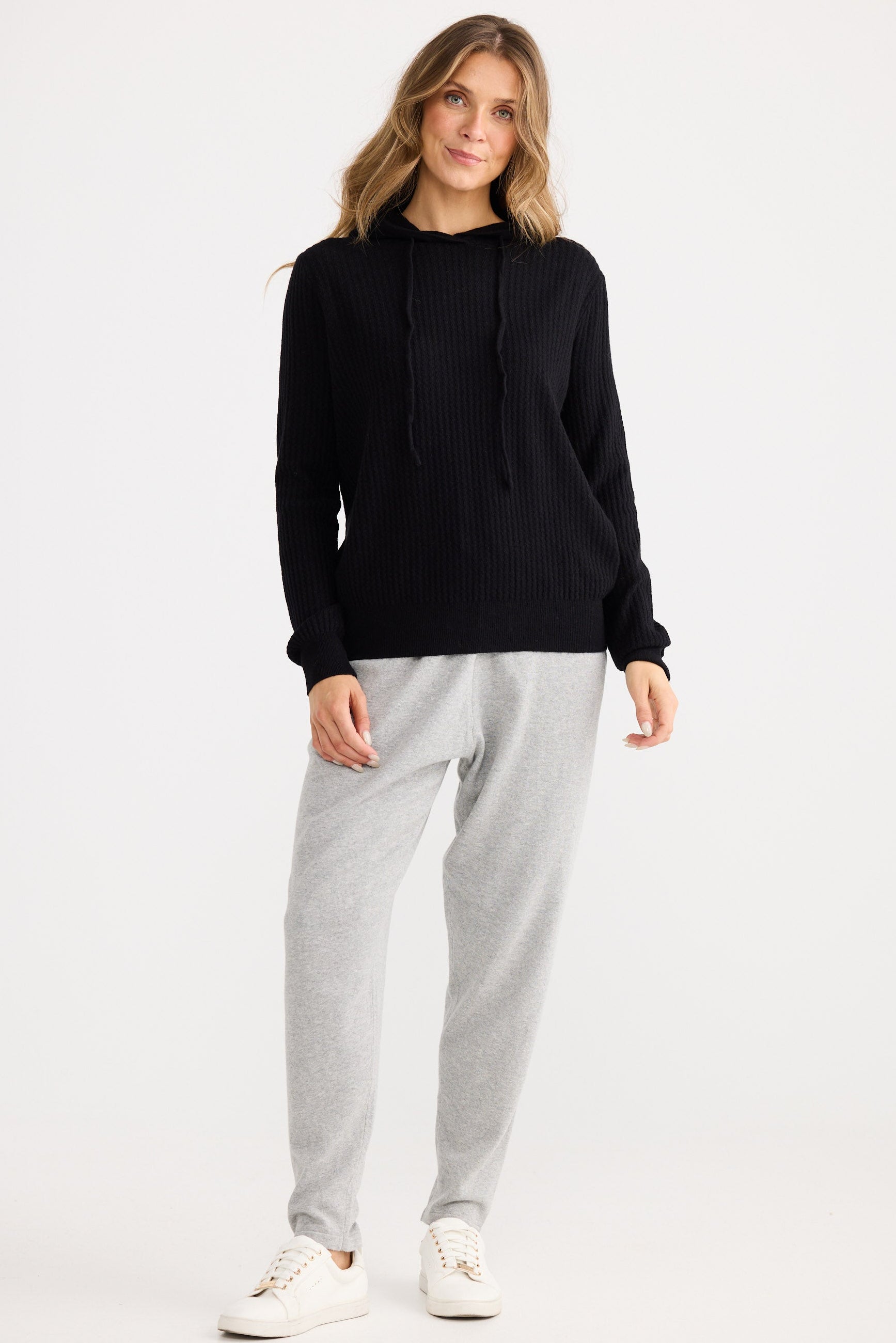 Woman wearing a black sweater and gray pants on a white background