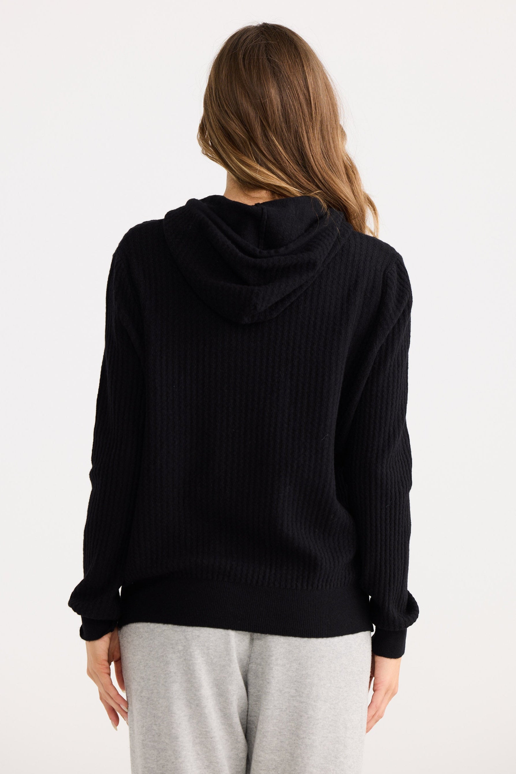 Person wearing a black hoodie and light gray pants on a white background