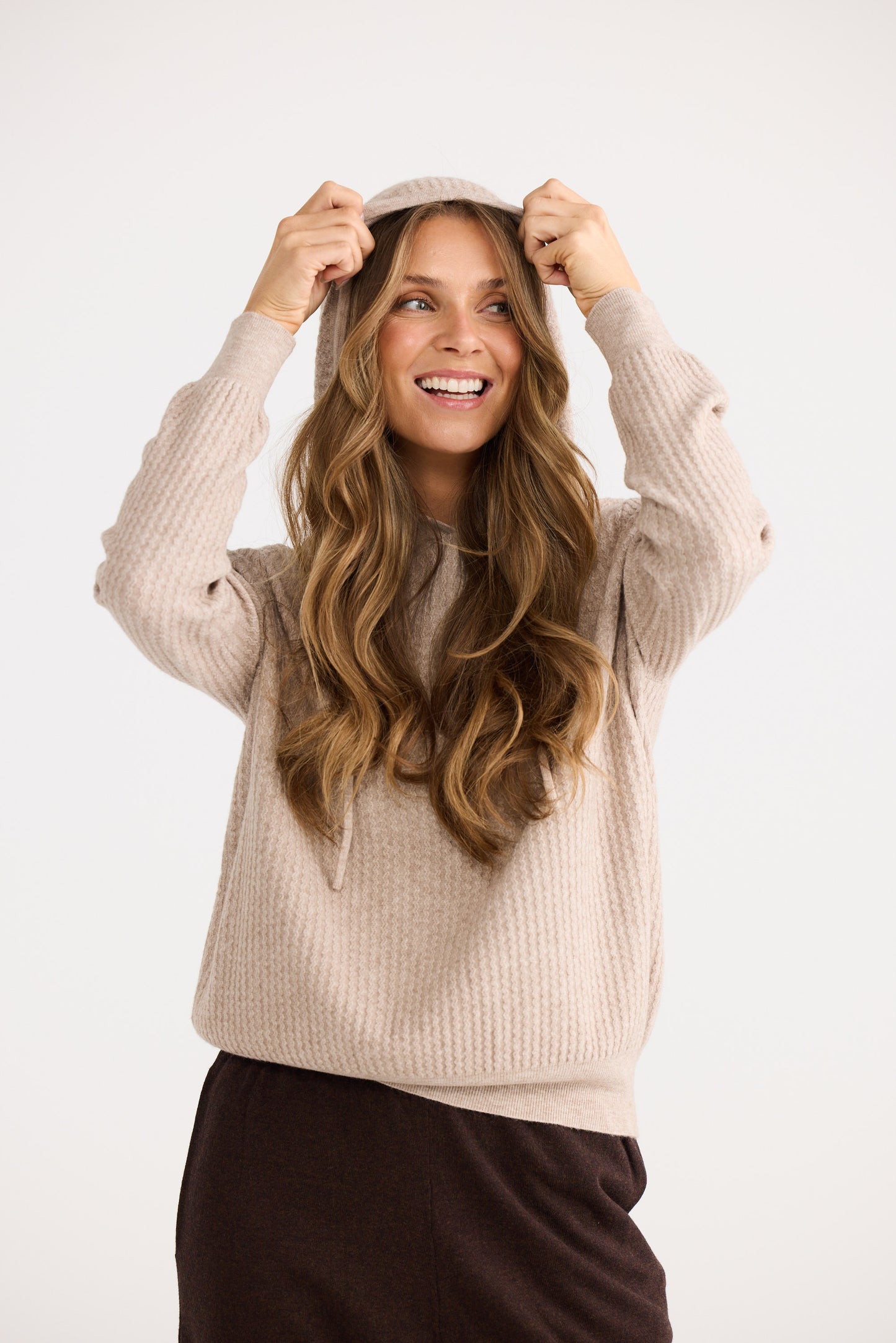 Woman wearing a beige sweater and black pants against a white background