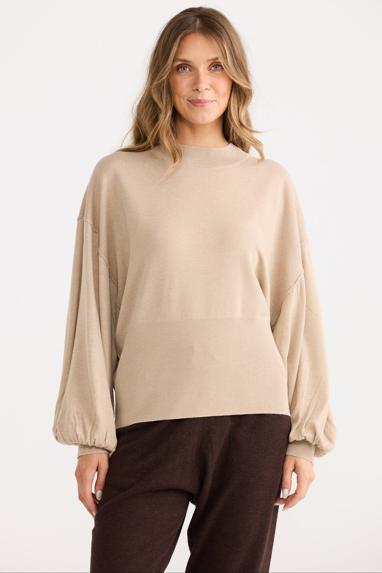 Woman wearing a beige sweater and brown pants on a white background