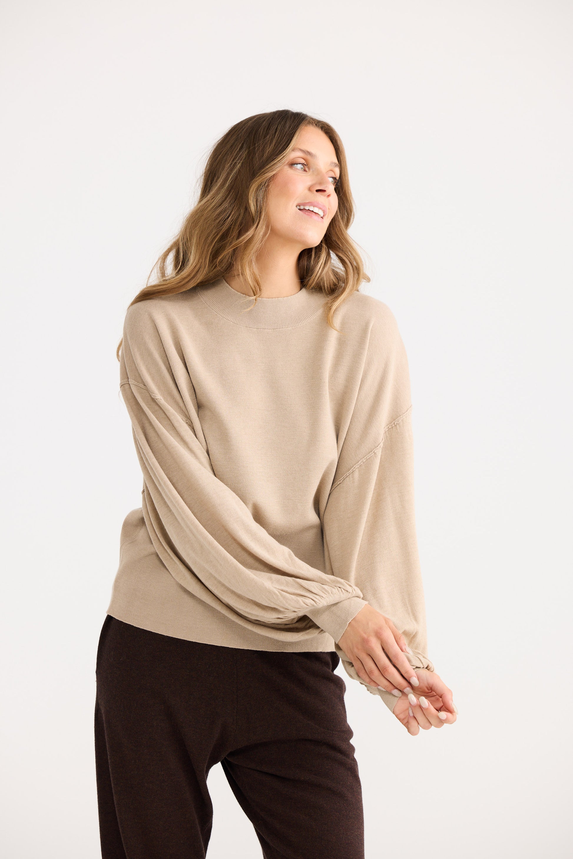 Woman wearing a beige sweater and brown pants on a white background