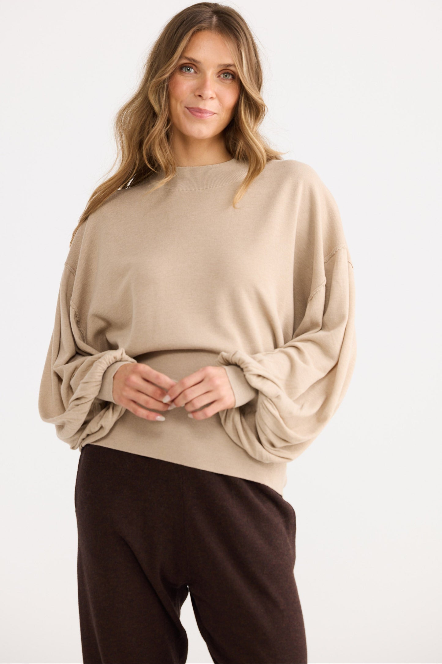 Woman wearing a beige sweater and brown pants on a white background