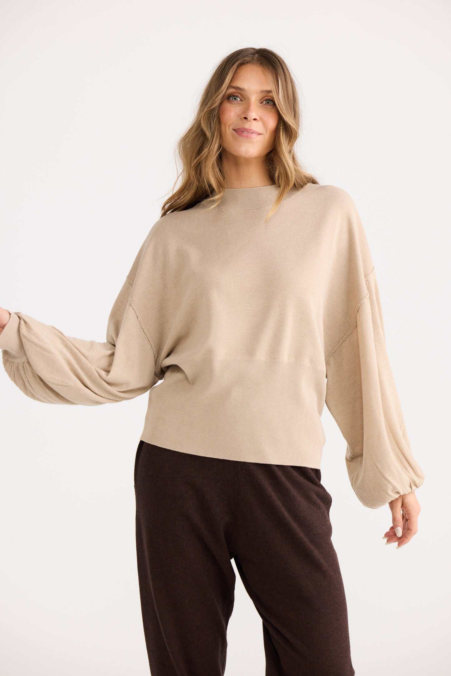 Woman wearing a beige sweater and brown pants on a white background