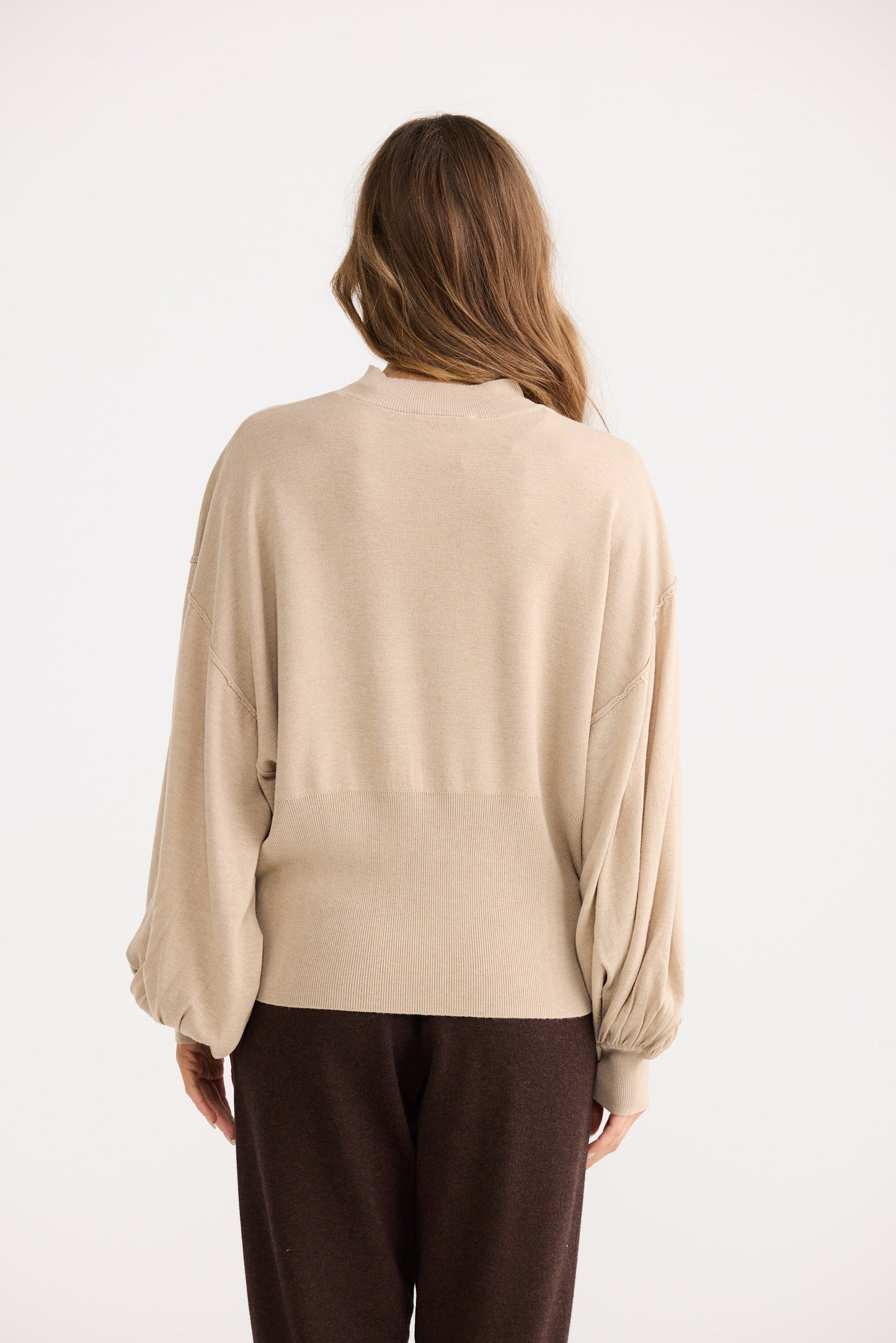 Woman wearing a beige blouse and brown pants on a white background