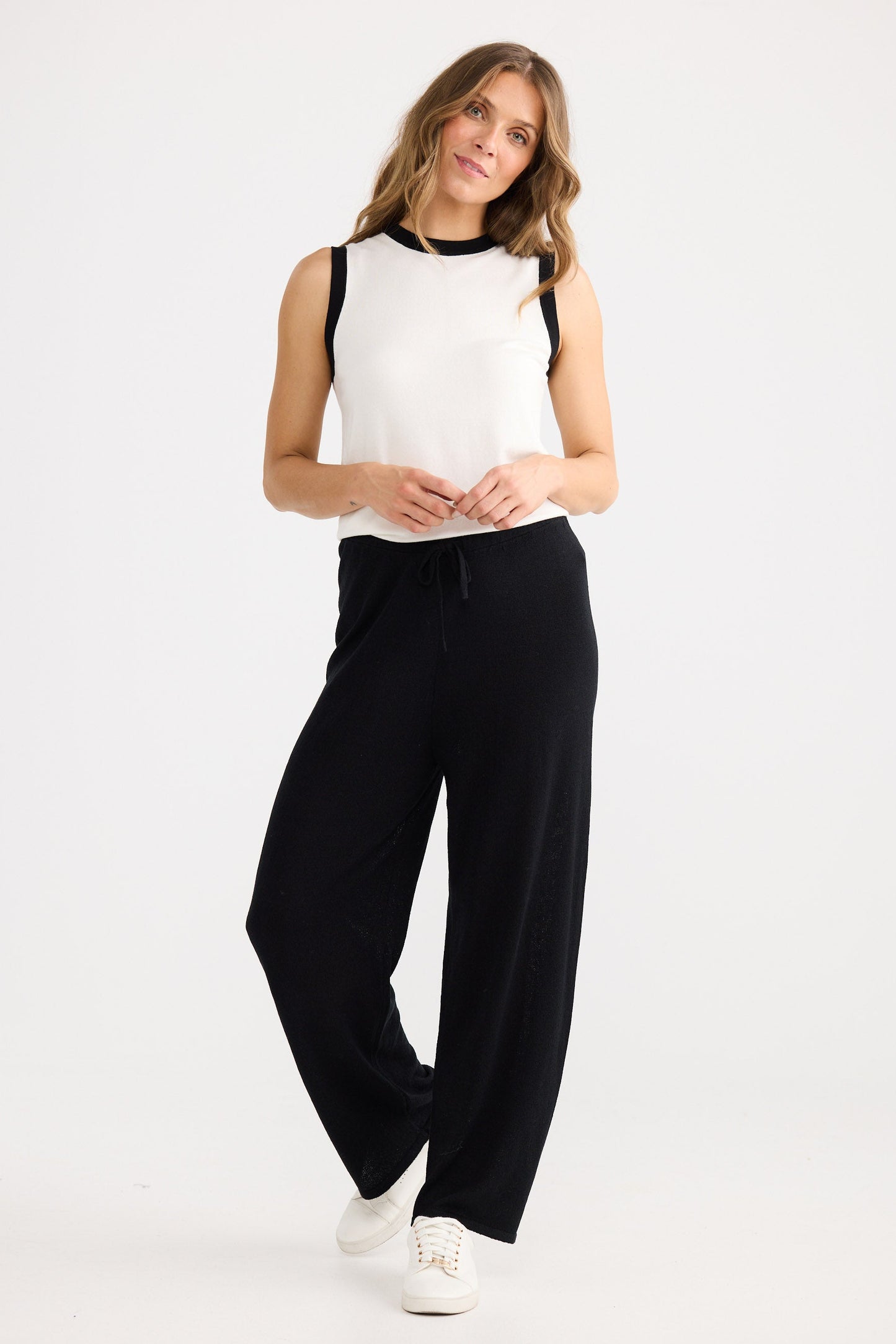 Woman wearing a white sleeveless top and black high-waisted pants on a white background