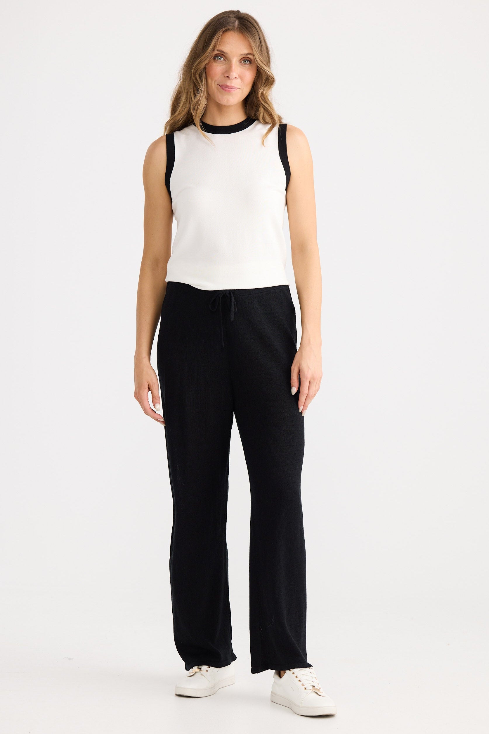 Woman wearing a white sleeveless top and black pants on a white background