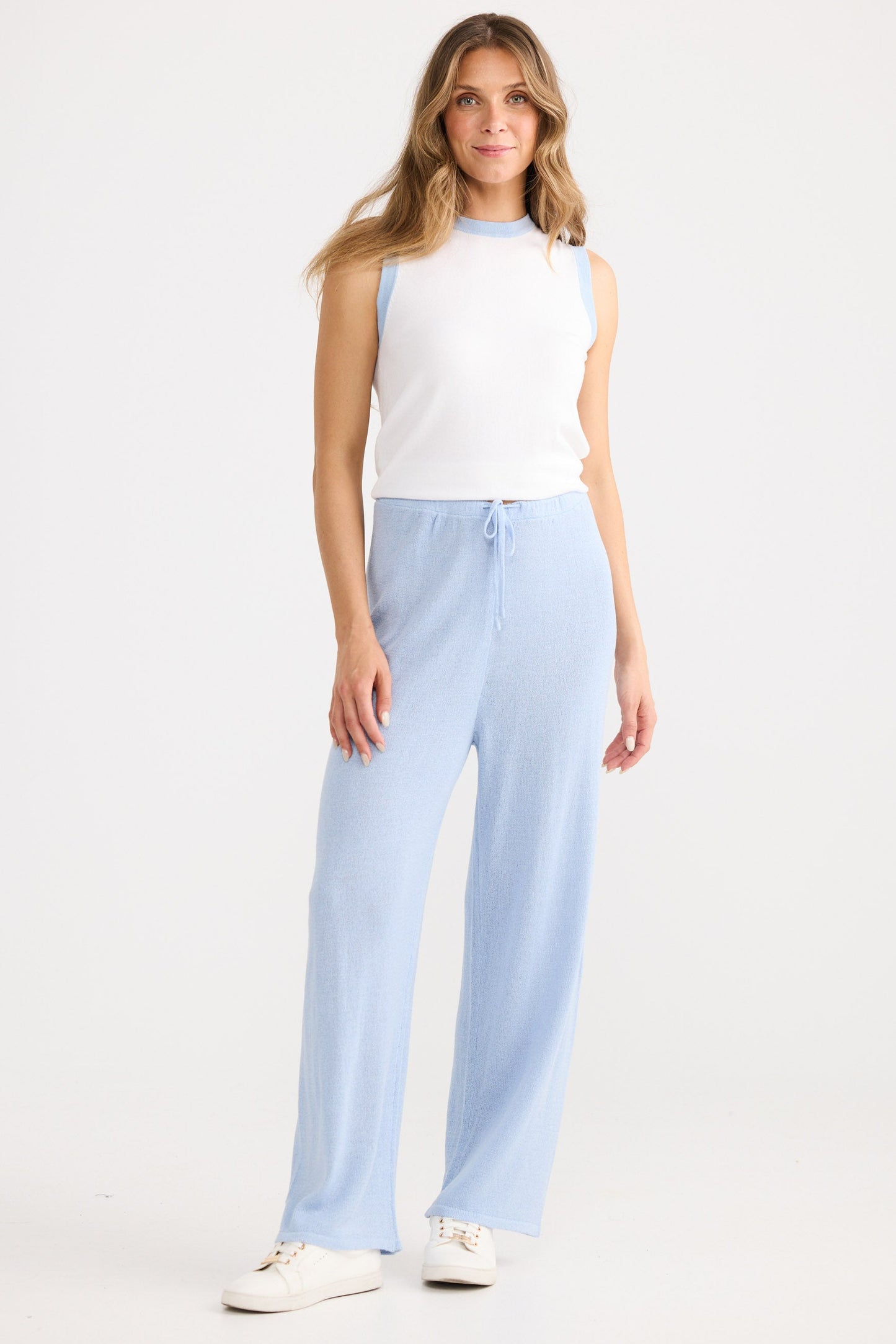 Woman wearing a white sleeveless top and light blue pants on a white background