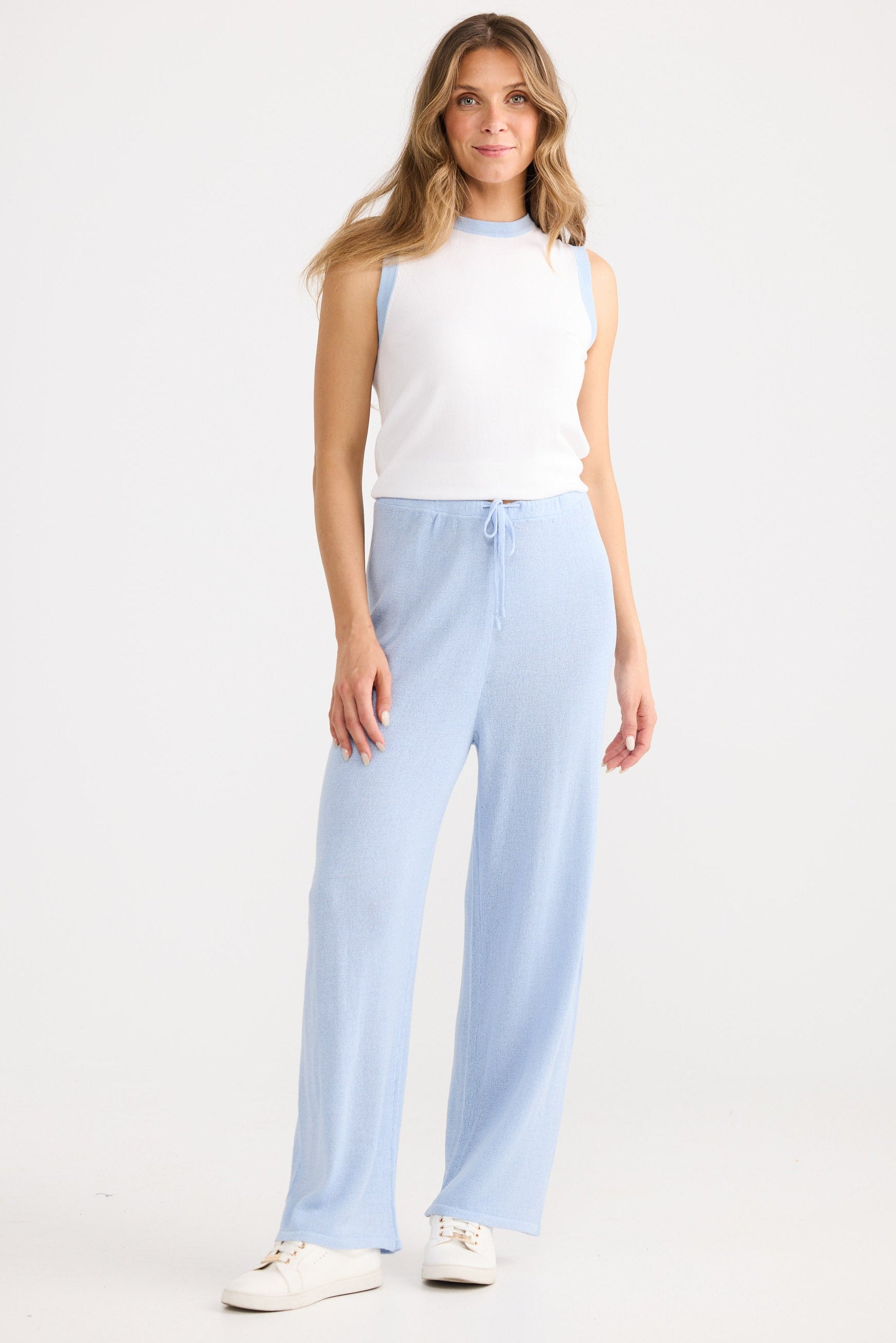 Woman wearing a white sleeveless top and light blue pants on a white background