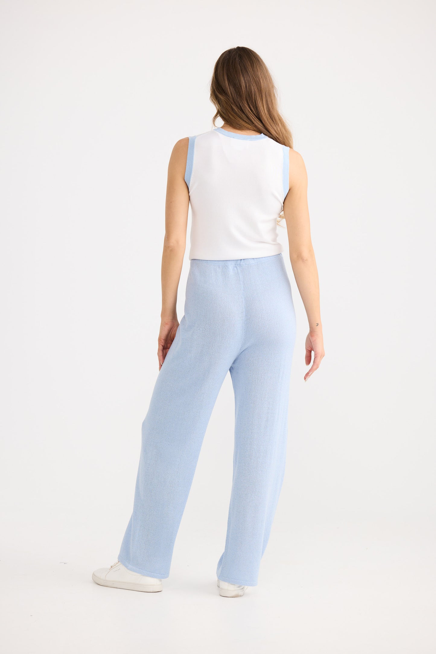 Woman wearing light blue pants and a white top on a white background