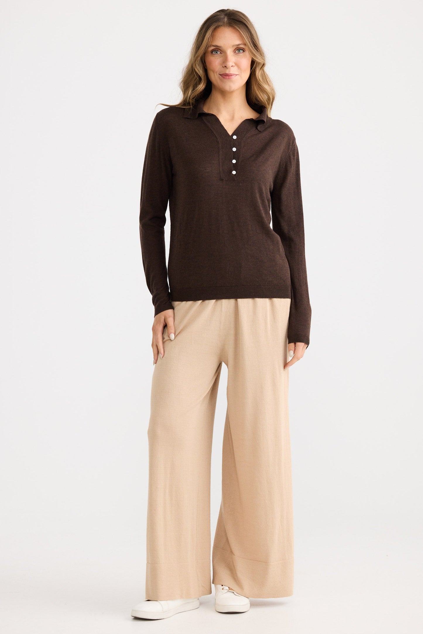 Woman wearing a brown long-sleeve shirt and beige wide-leg pants on a white background