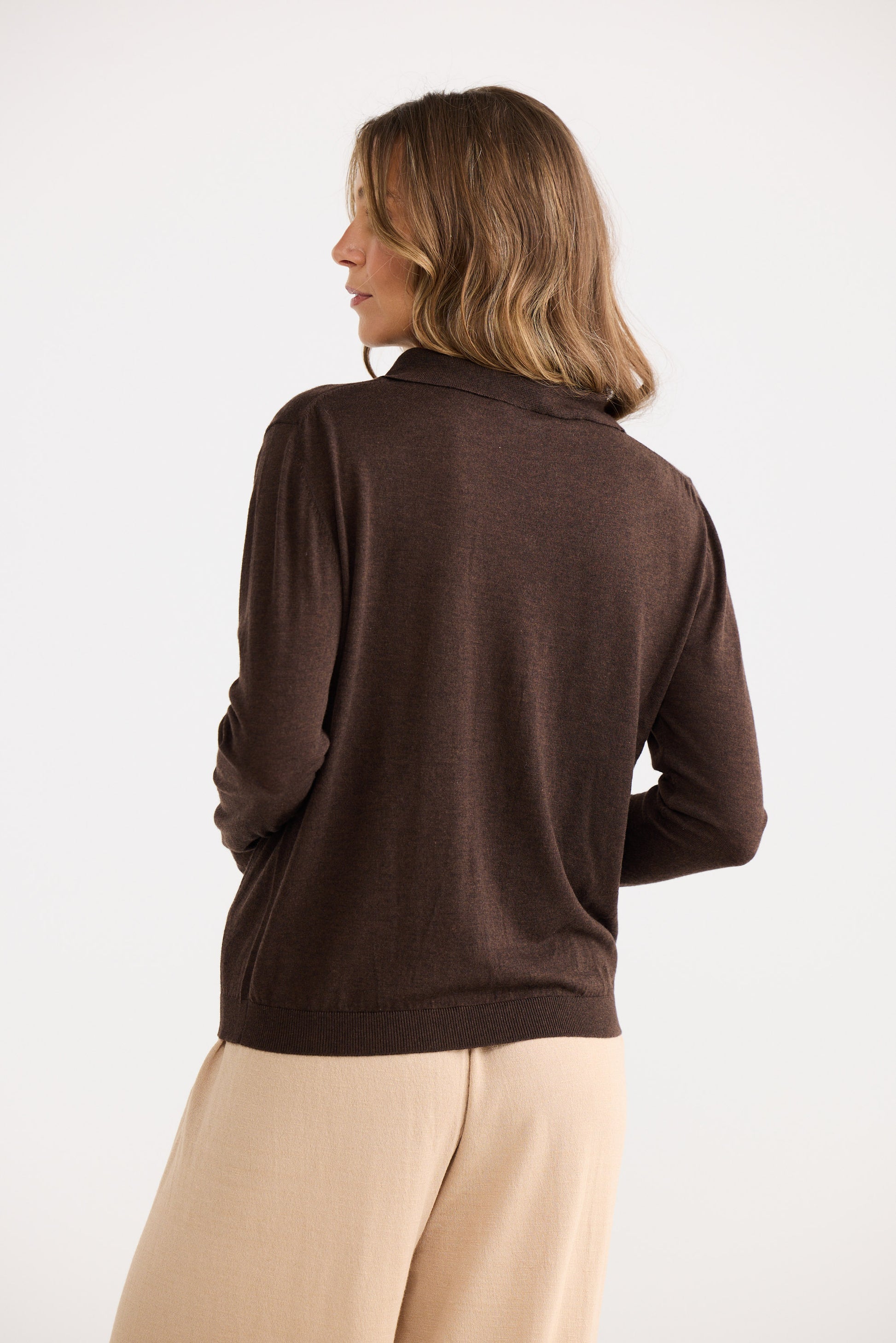 Woman wearing a brown sweater and beige pants on a white background