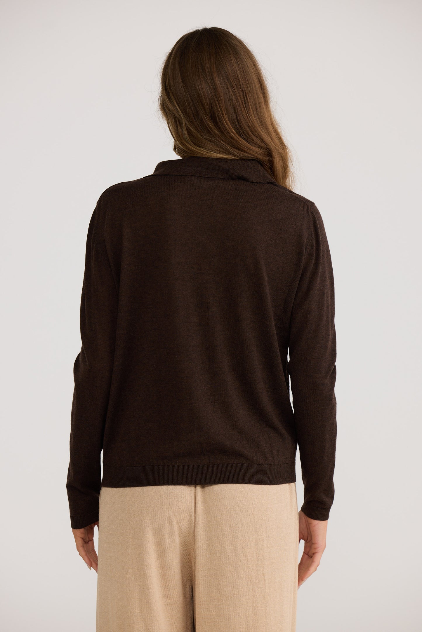 Person wearing a brown sweater and beige pants against a white background