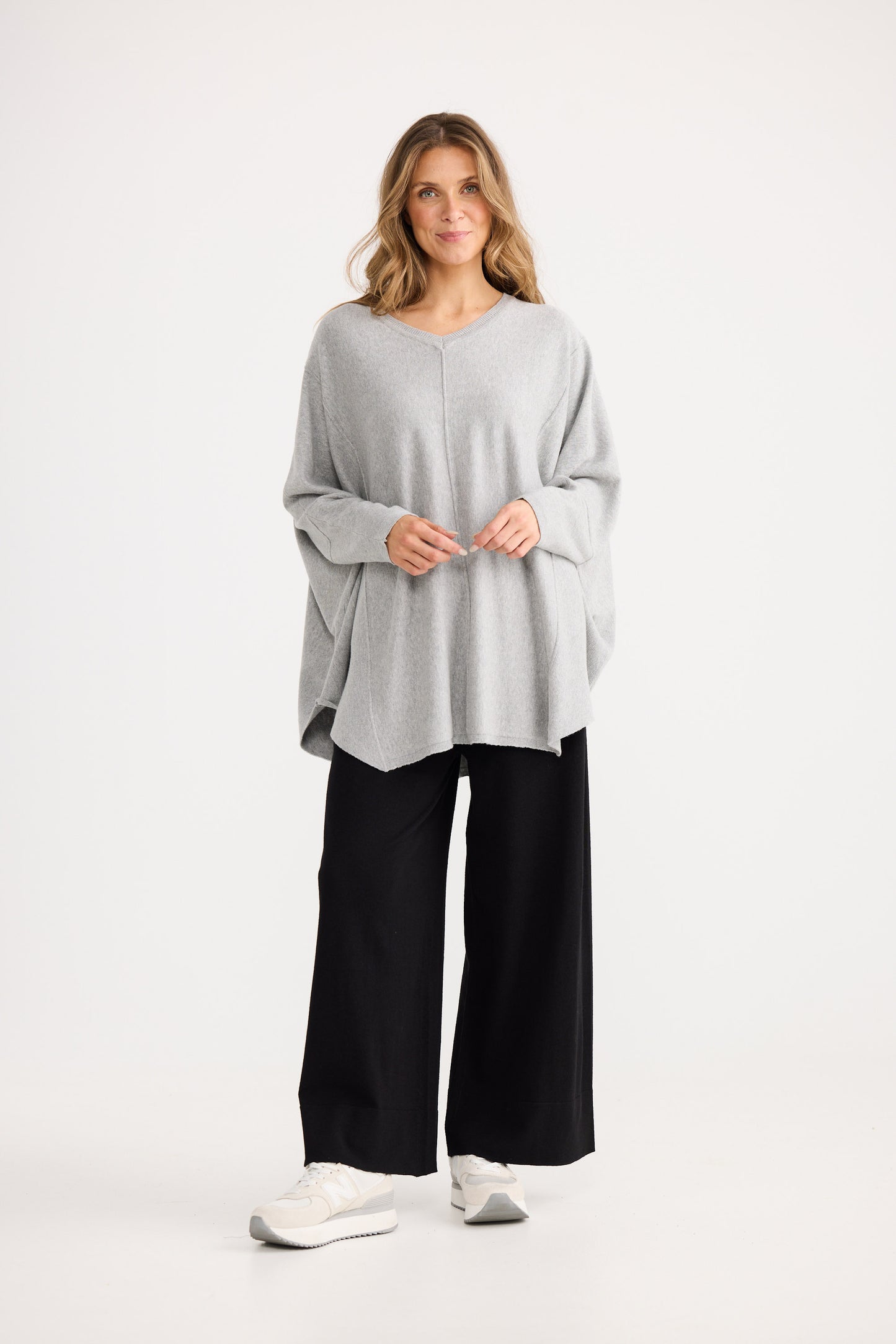 Woman wearing a light gray oversized sweater and black pants on a white background