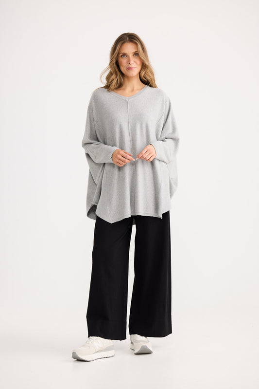 Woman wearing a light gray oversized sweater and black pants on a white background