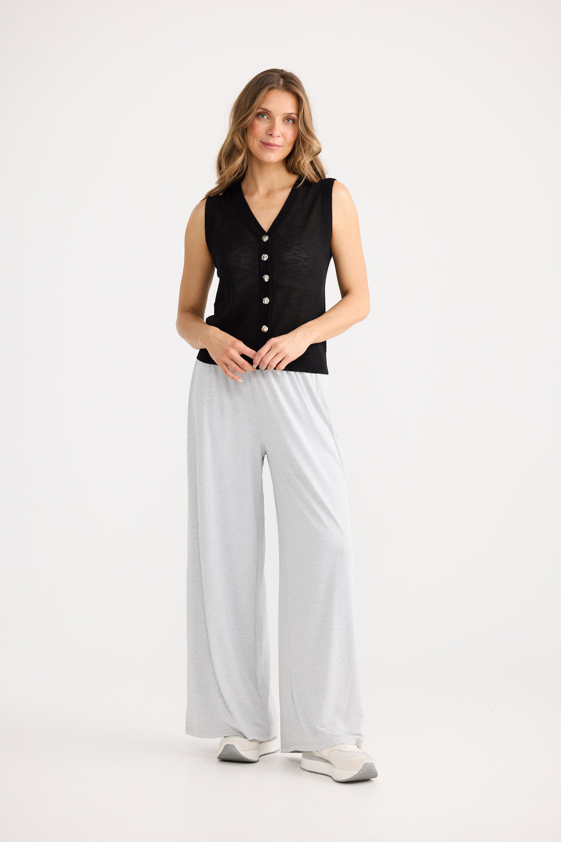 Woman wearing a black sleeveless top and white pants on a white background
