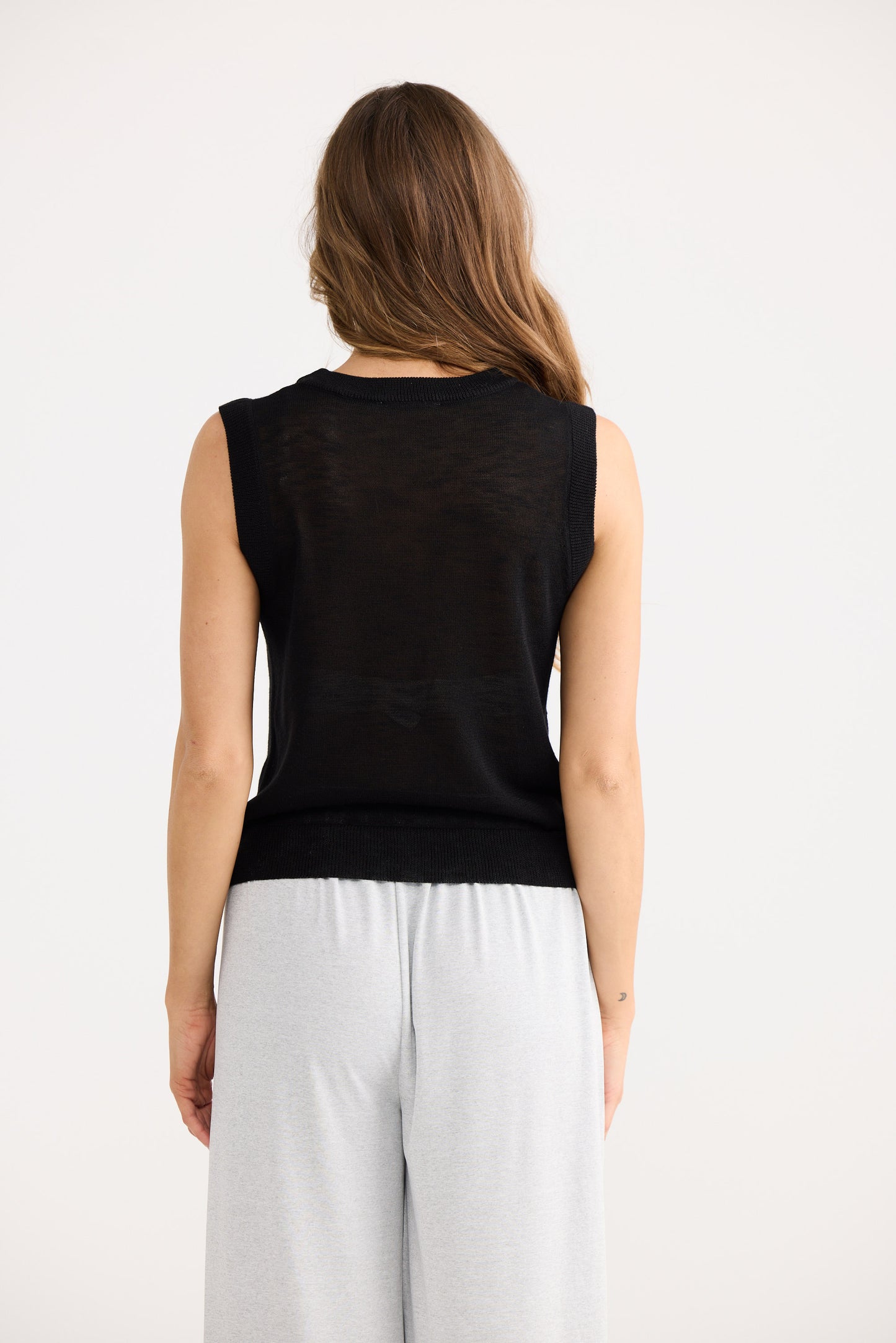 Woman wearing a black sleeveless top and white pants on a white background