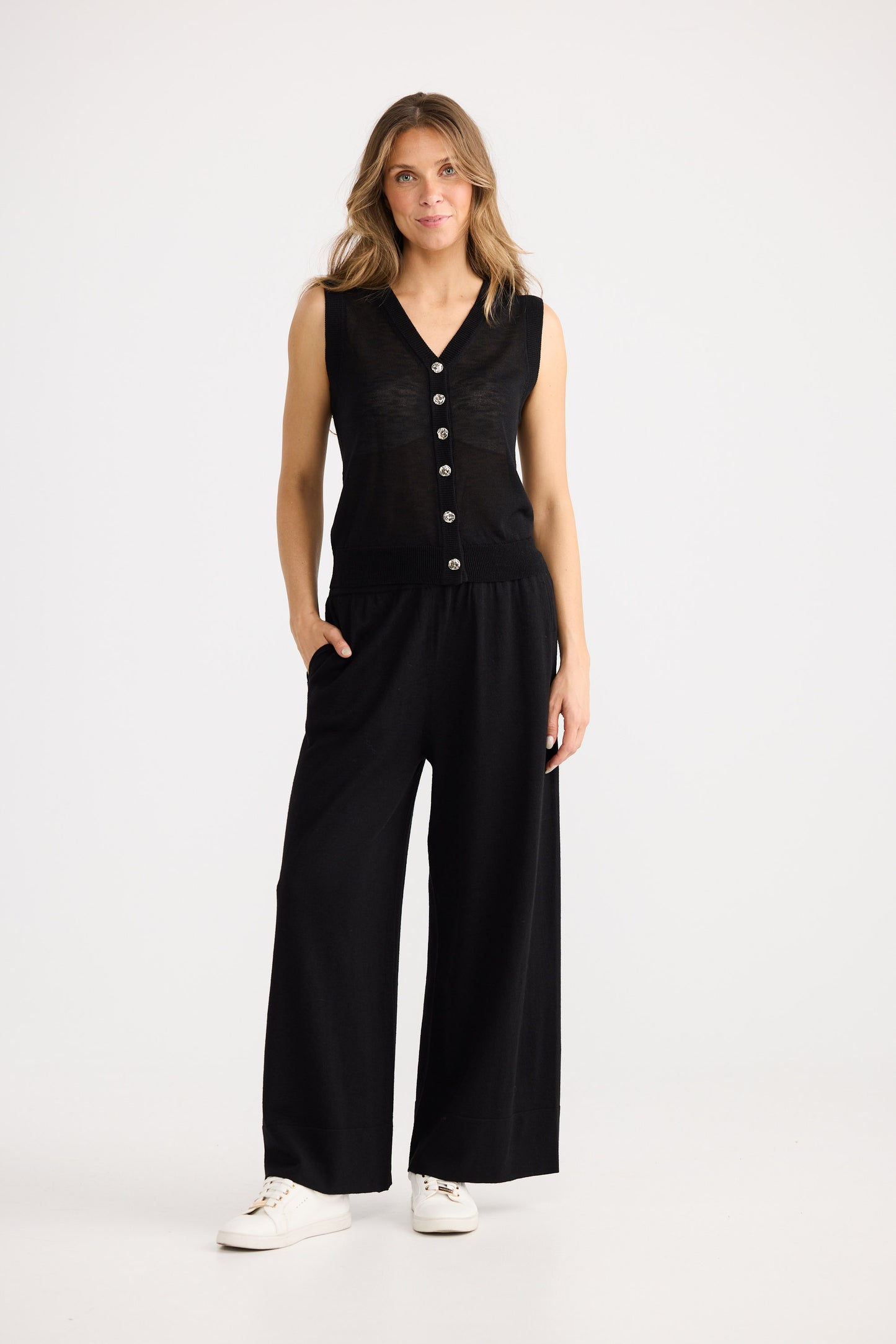Woman wearing a black sleeveless jumpsuit with buttons on a white background